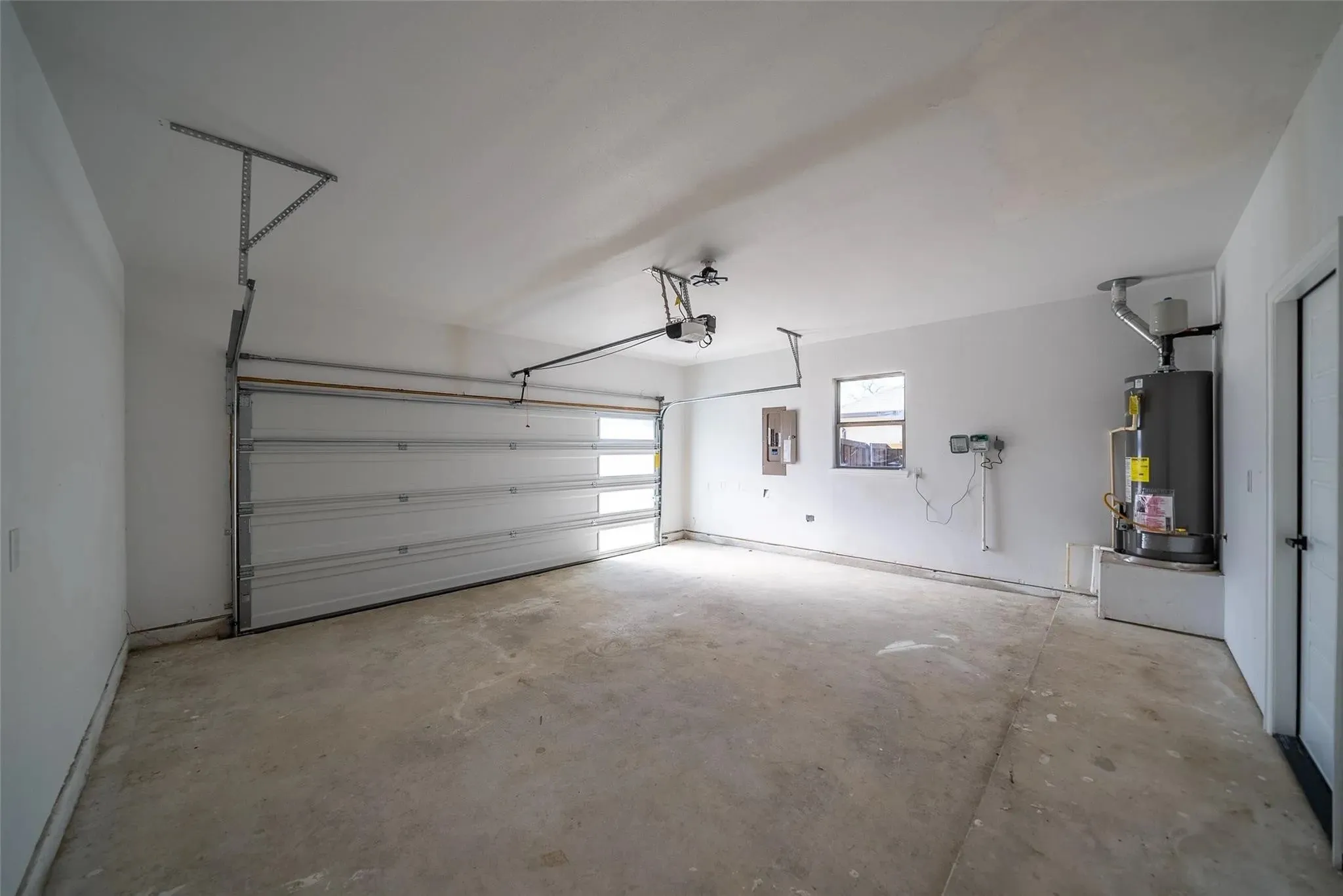 Spacious garage featuring a concrete floor, an overhead door with frosted glass panels, an automatic opener, a water heater, and a side window