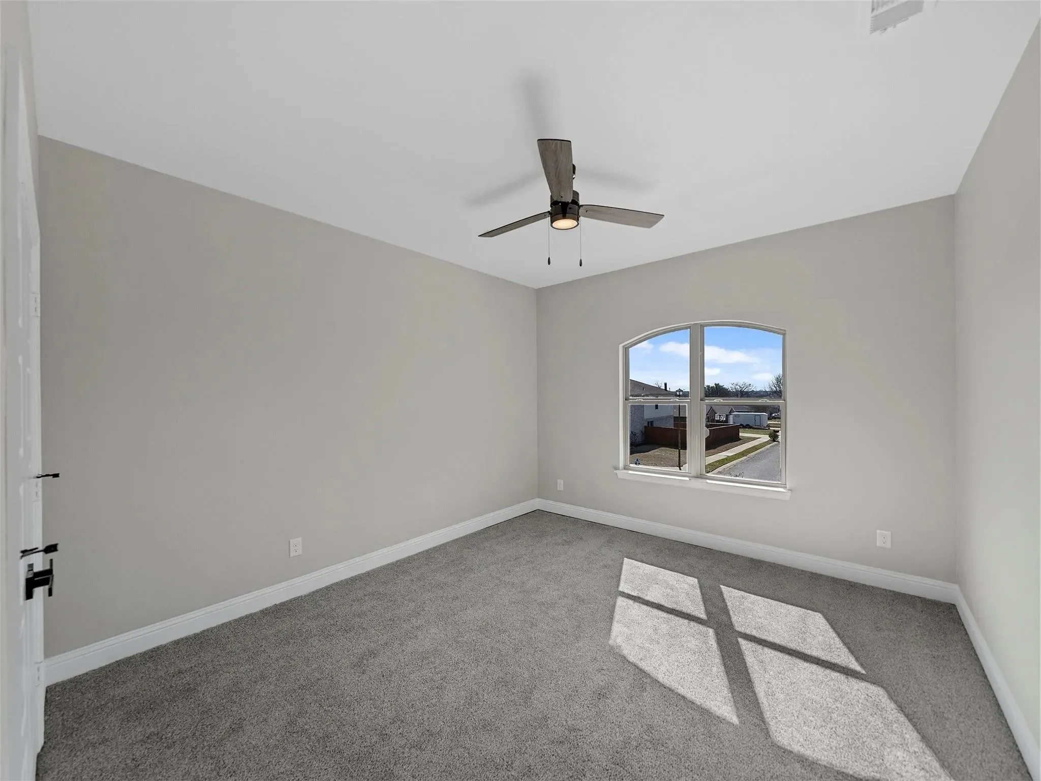 Carpeted room featuring light gray walls, a window with an arched top, a ceiling fan with light fixture, and white baseboards