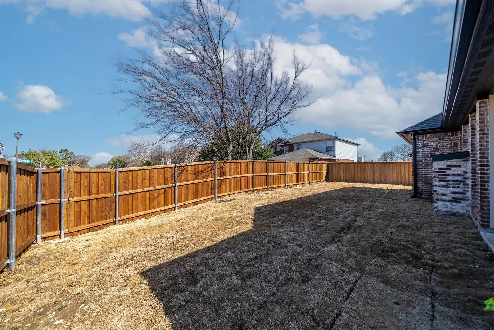 Spacious backyard featuring a new wood privacy fence with metal posts, a brick and stone exterior, and a dark shingle roof with matching gutters