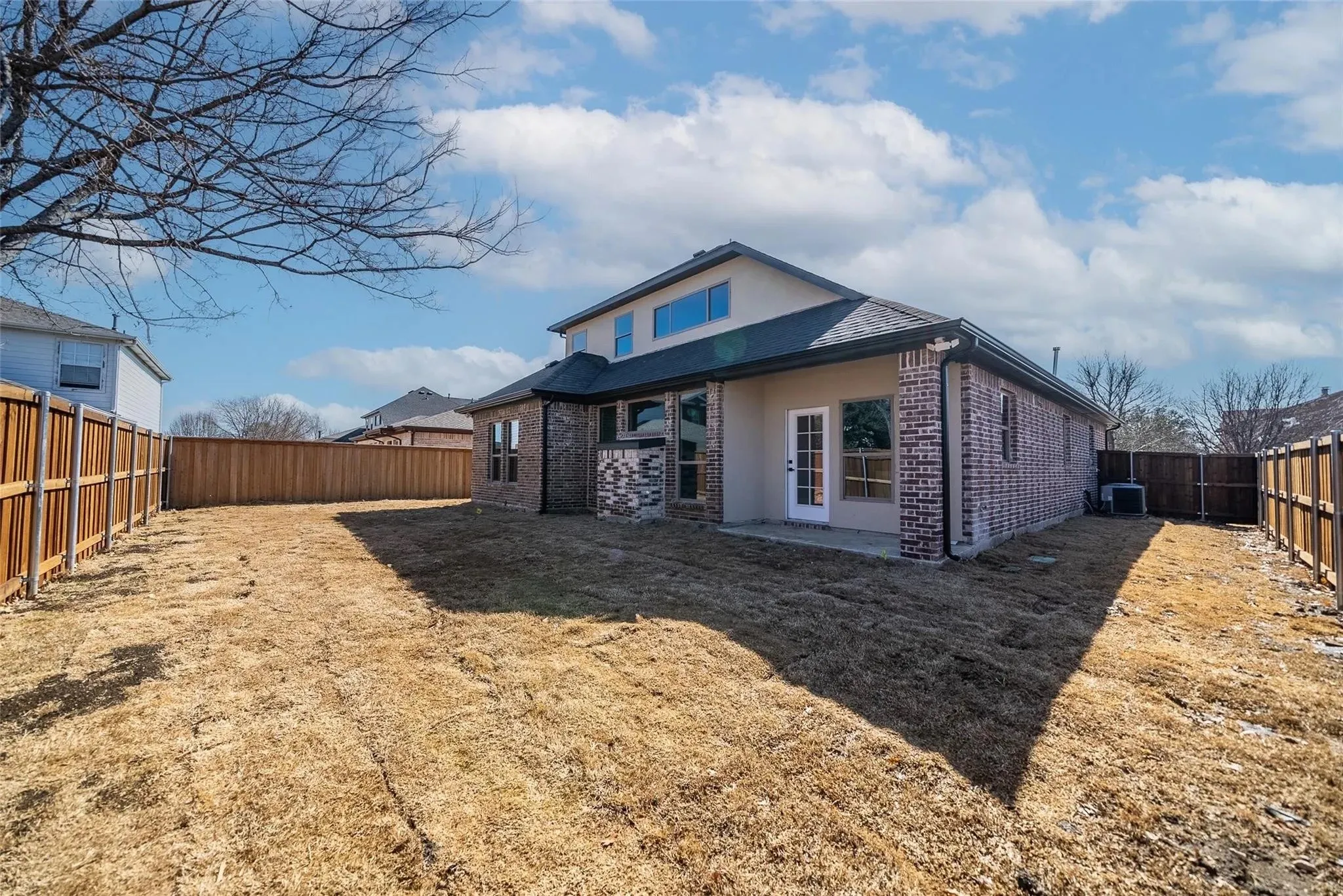 Spacious backyard featuring a brick and stucco exterior, multiple large windows, a rear patio with French doors, and a full privacy fence