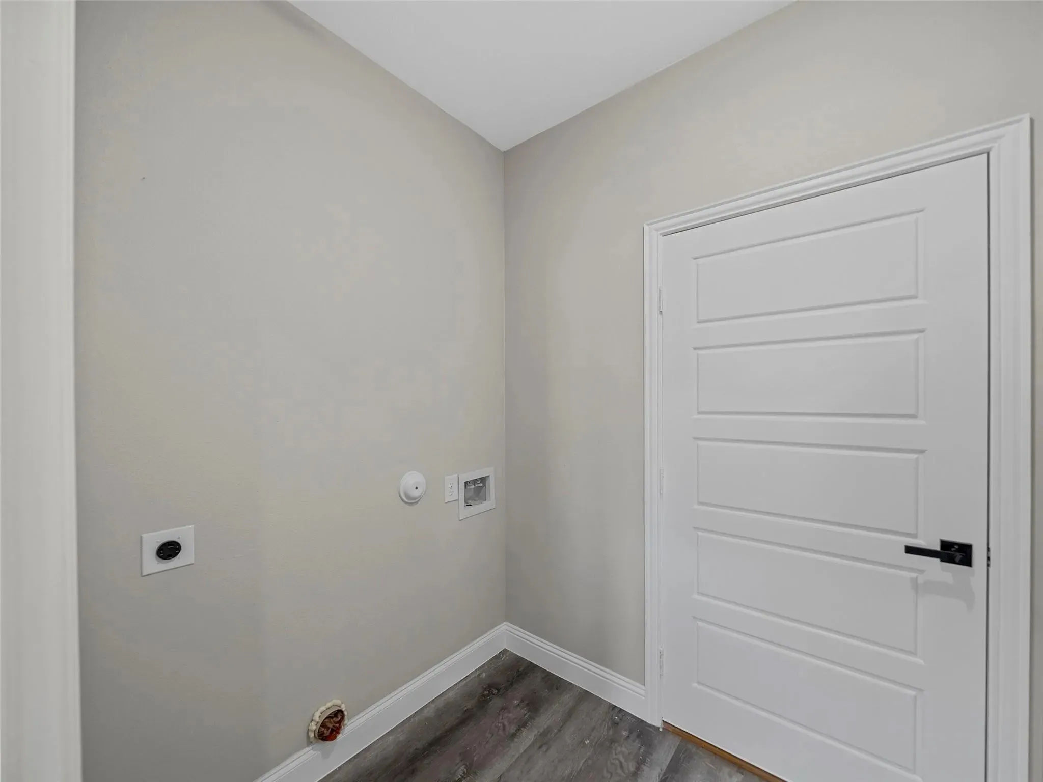 Utility area featuring wood-finish flooring, light gray walls, a modern five-panel interior door with matte black hardware, and essential hookups