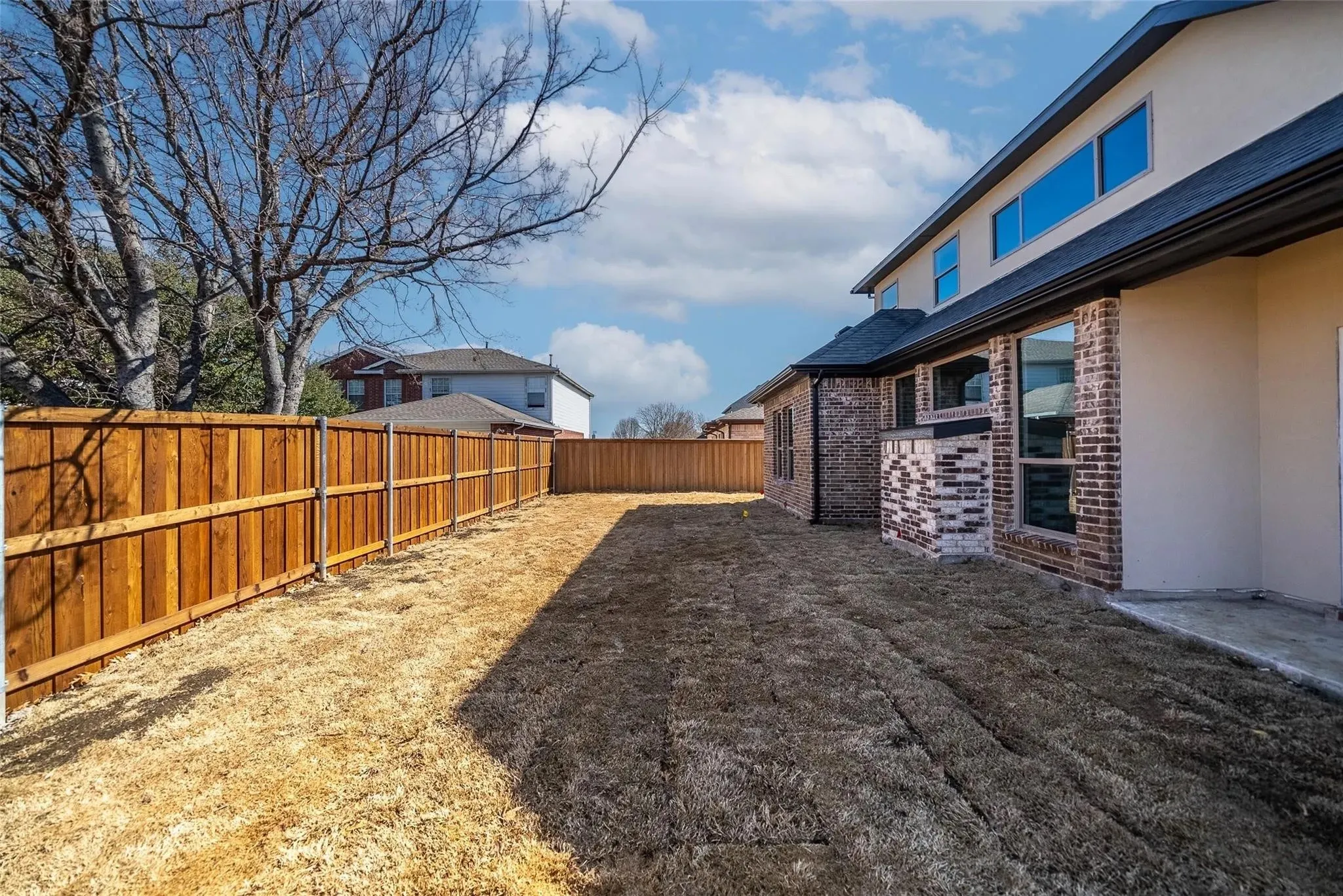 Expansive backyard with a newly installed wood privacy fence, brick and stucco exterior, multiple large windows, and a concrete patio pad