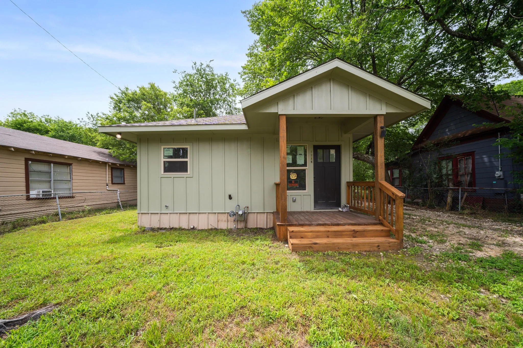Light green siding with a front porch entry, wood-finish porch railings, and a dark entry door