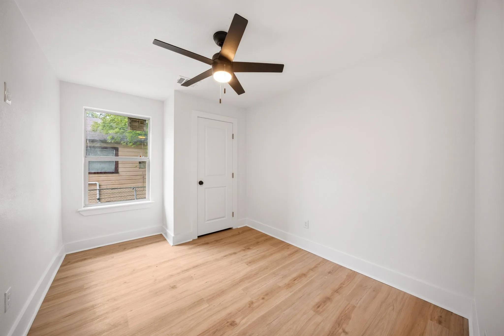 Bright room featuring wood-finish flooring, white walls, and a modern ceiling fan with integrated lighting