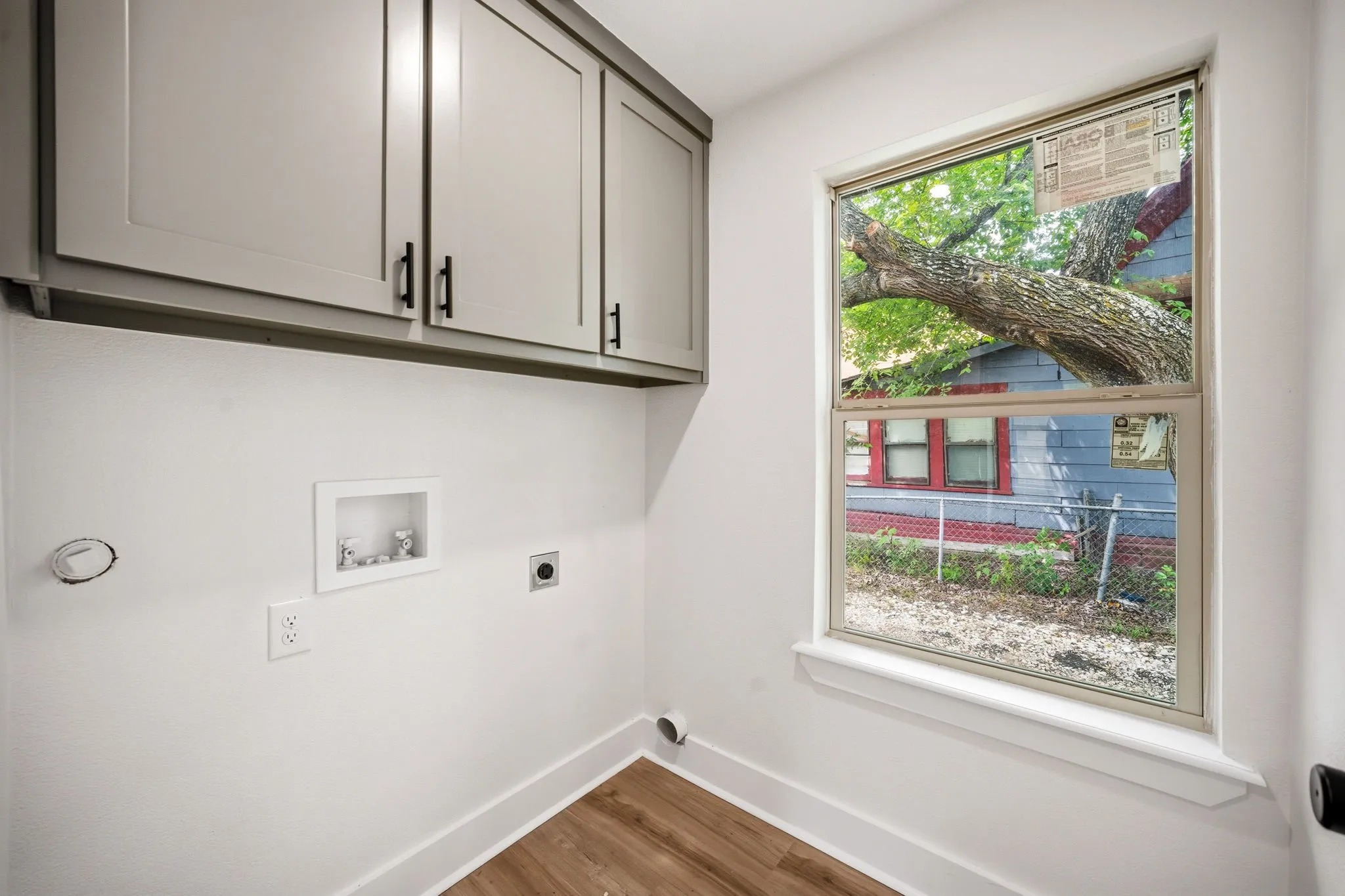 Laundry area featuring light gray shaker-style cabinetry with matte black hardware, wood-finish flooring, and a double-hung window