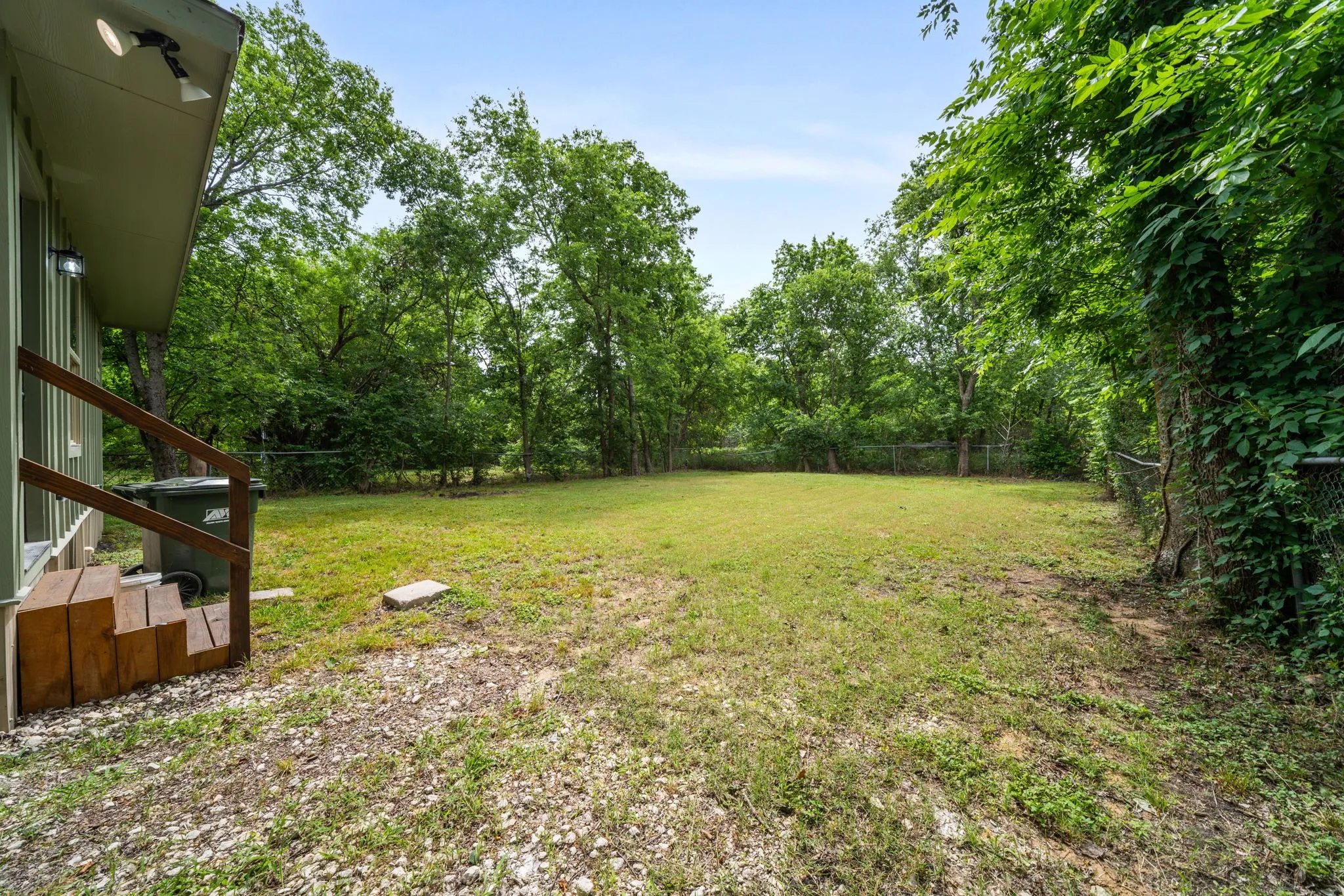 Generous backyard featuring mature perimeter trees, a chain-link fence, and natural landscaping