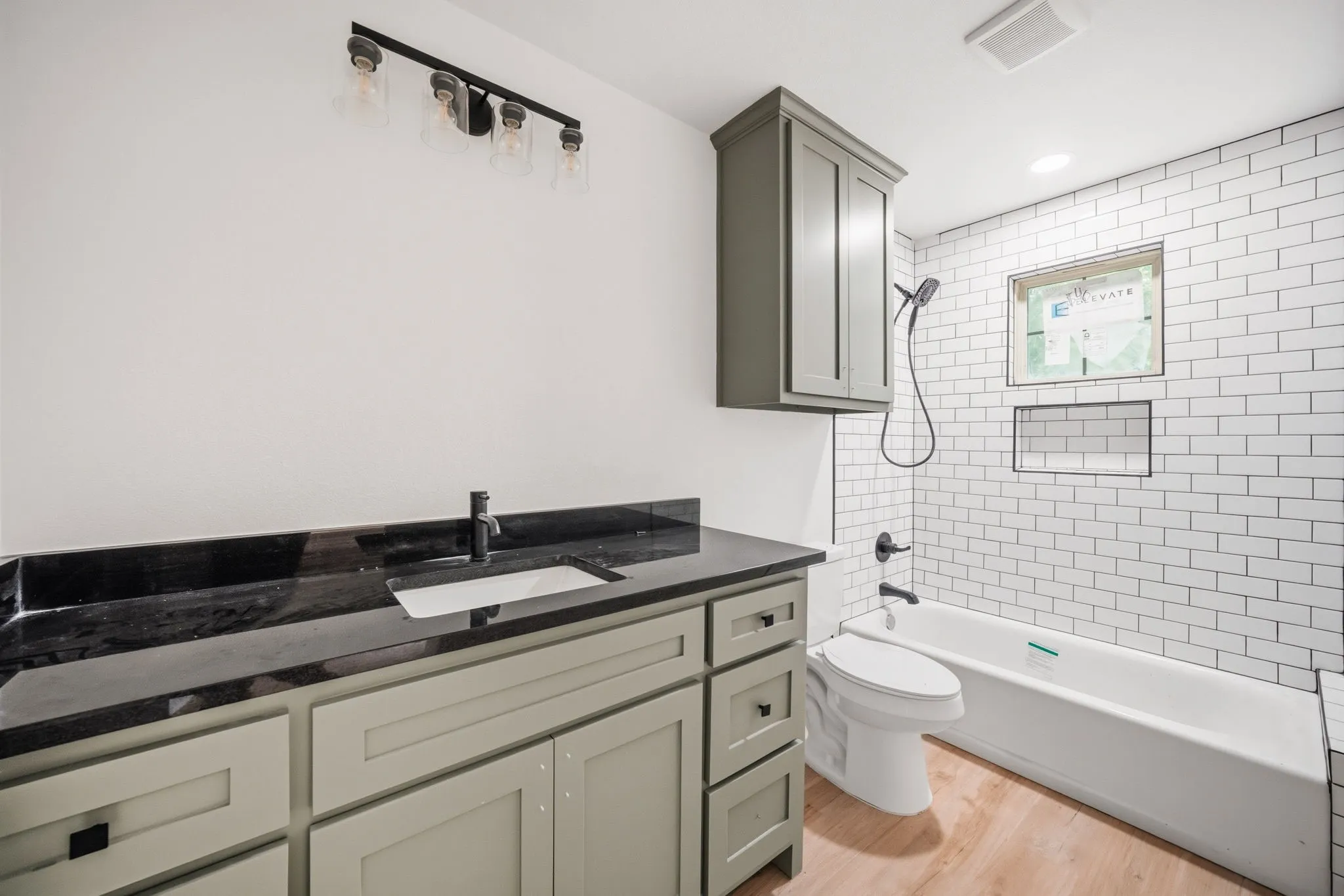 Bathroom featuring a light-toned wood-finish floor, a gray vanity with a dark countertop and integrated sink, and a black faucet