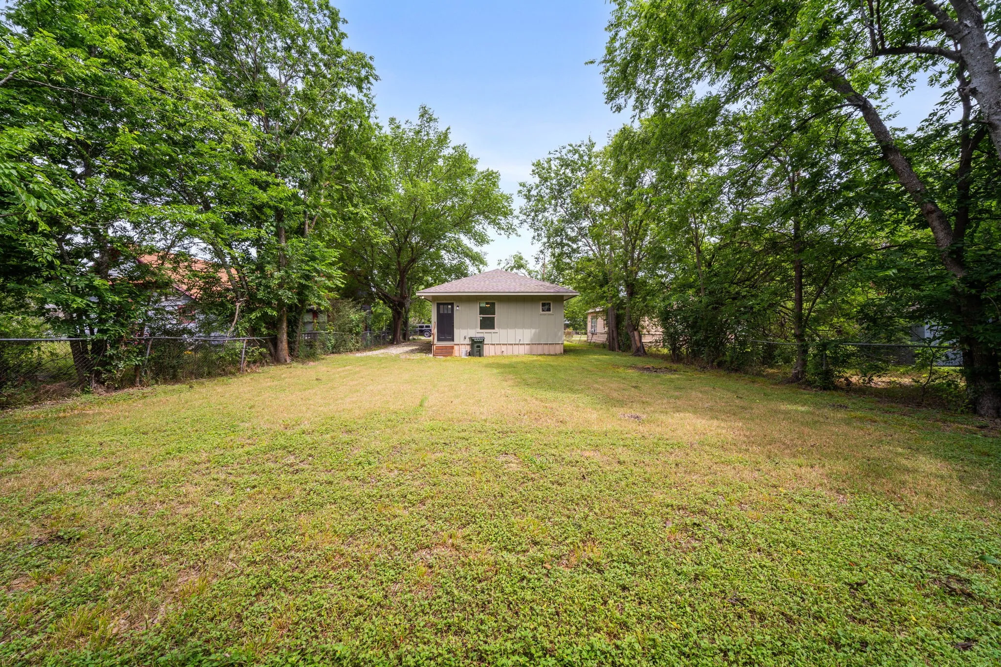 Expansive rear yard featuring green lawn, mature perimeter trees, and a chain-link fence