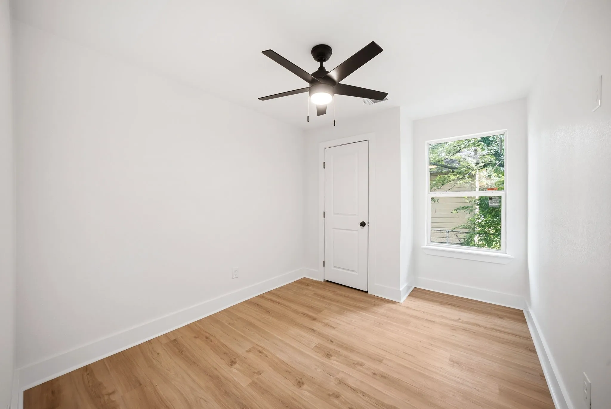 Bright room featuring light wood-finish flooring, white walls, and a modern ceiling fan