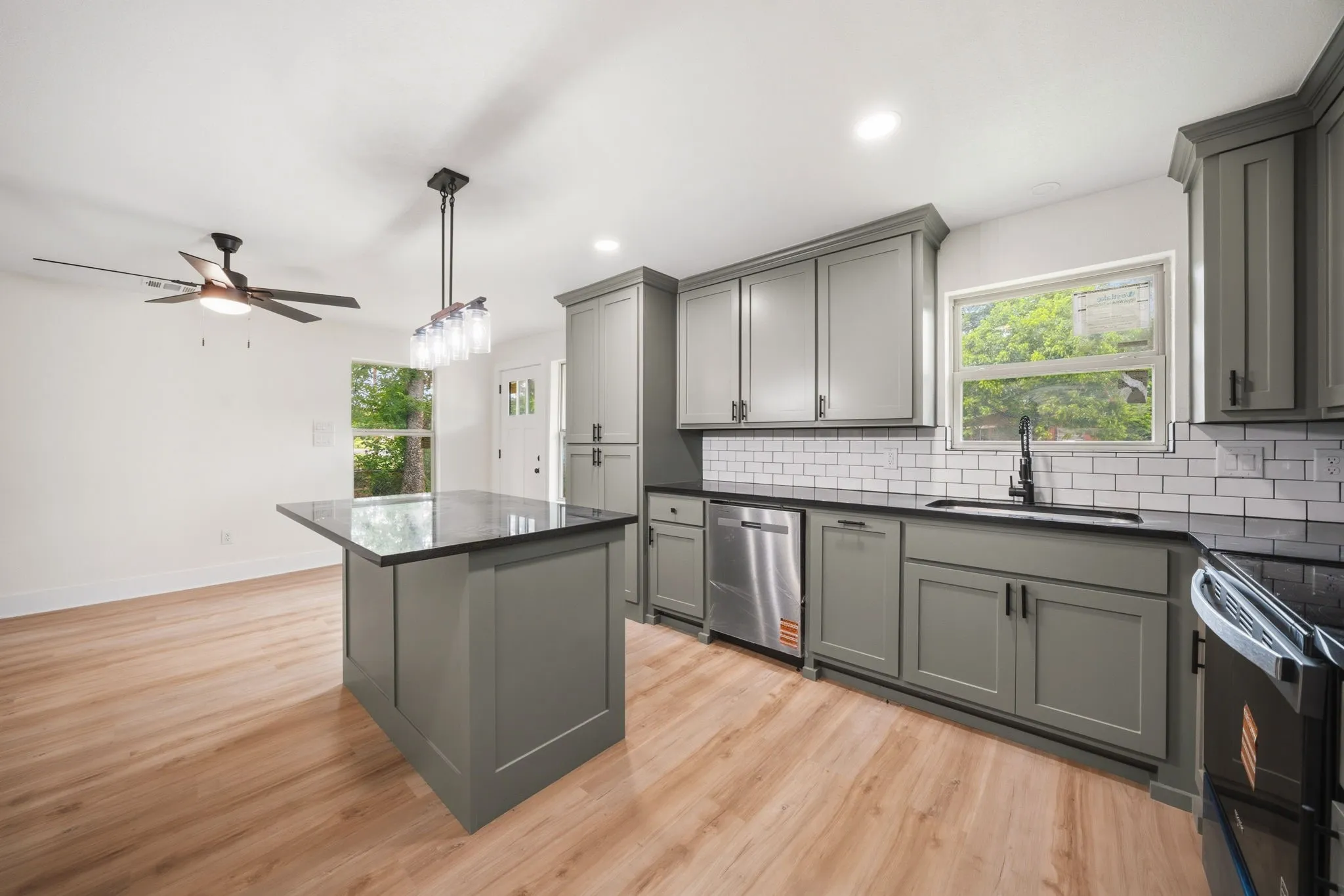 Open-concept kitchen featuring an island with a dark countertop, grey shaker cabinetry, stainless steel appliances, white subway tile backsplash, and wood-finish flooring