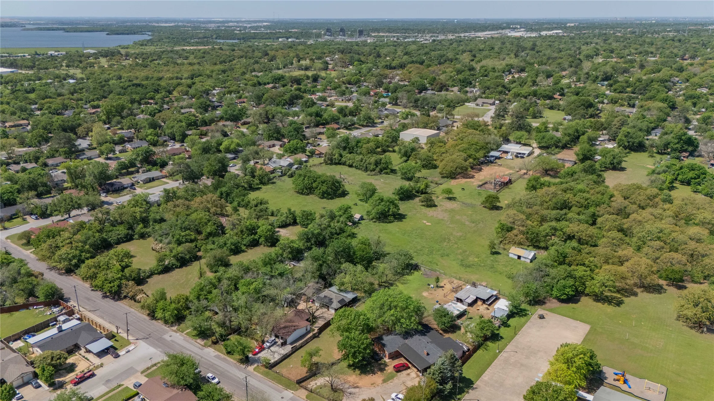 Expansive aerial landscape featuring a large body of water, numerous mature trees, and residential properties