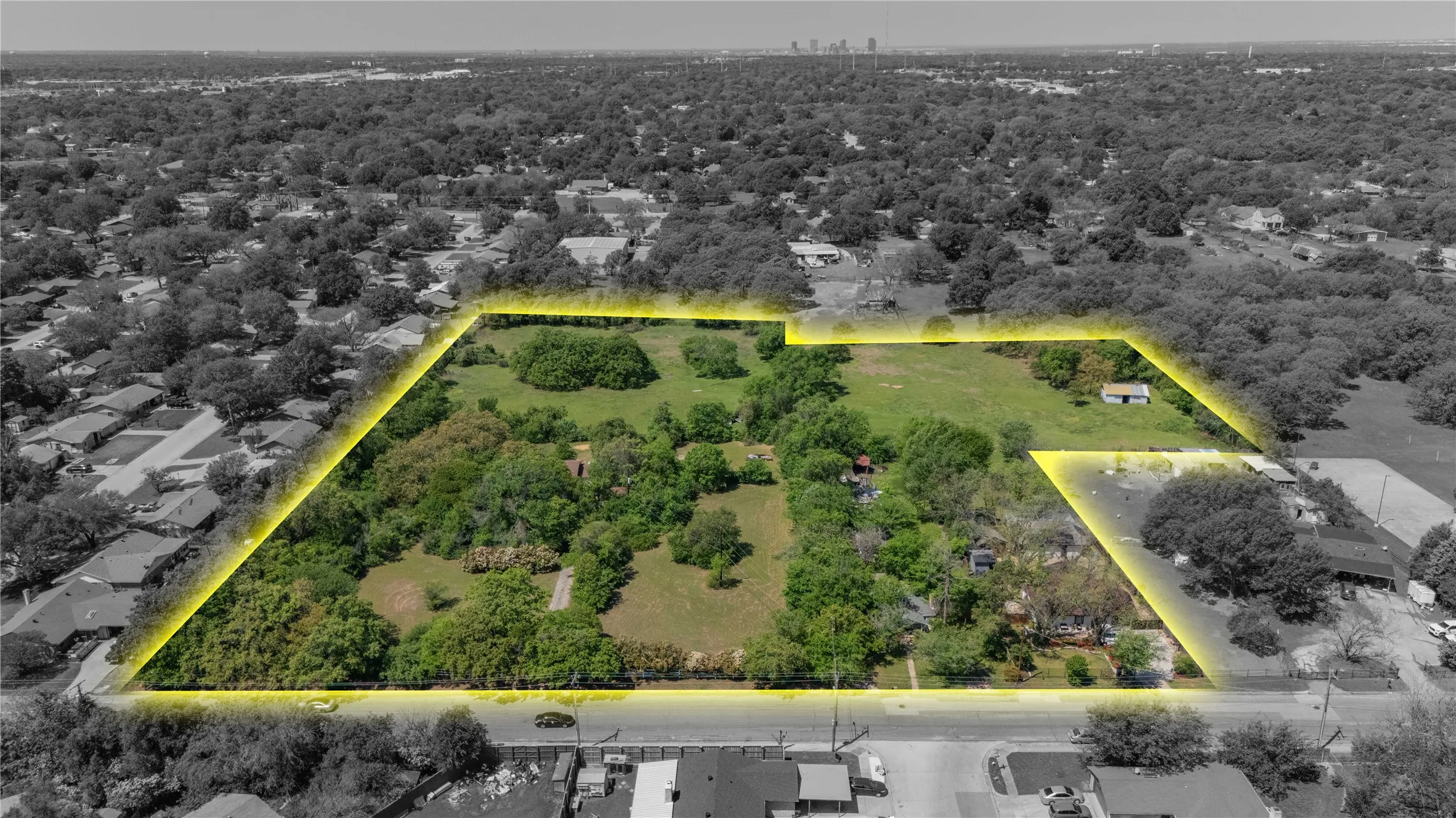 Expansive land parcel featuring a mixture of open grassy areas and mature trees, bordered by residential properties and a roadway