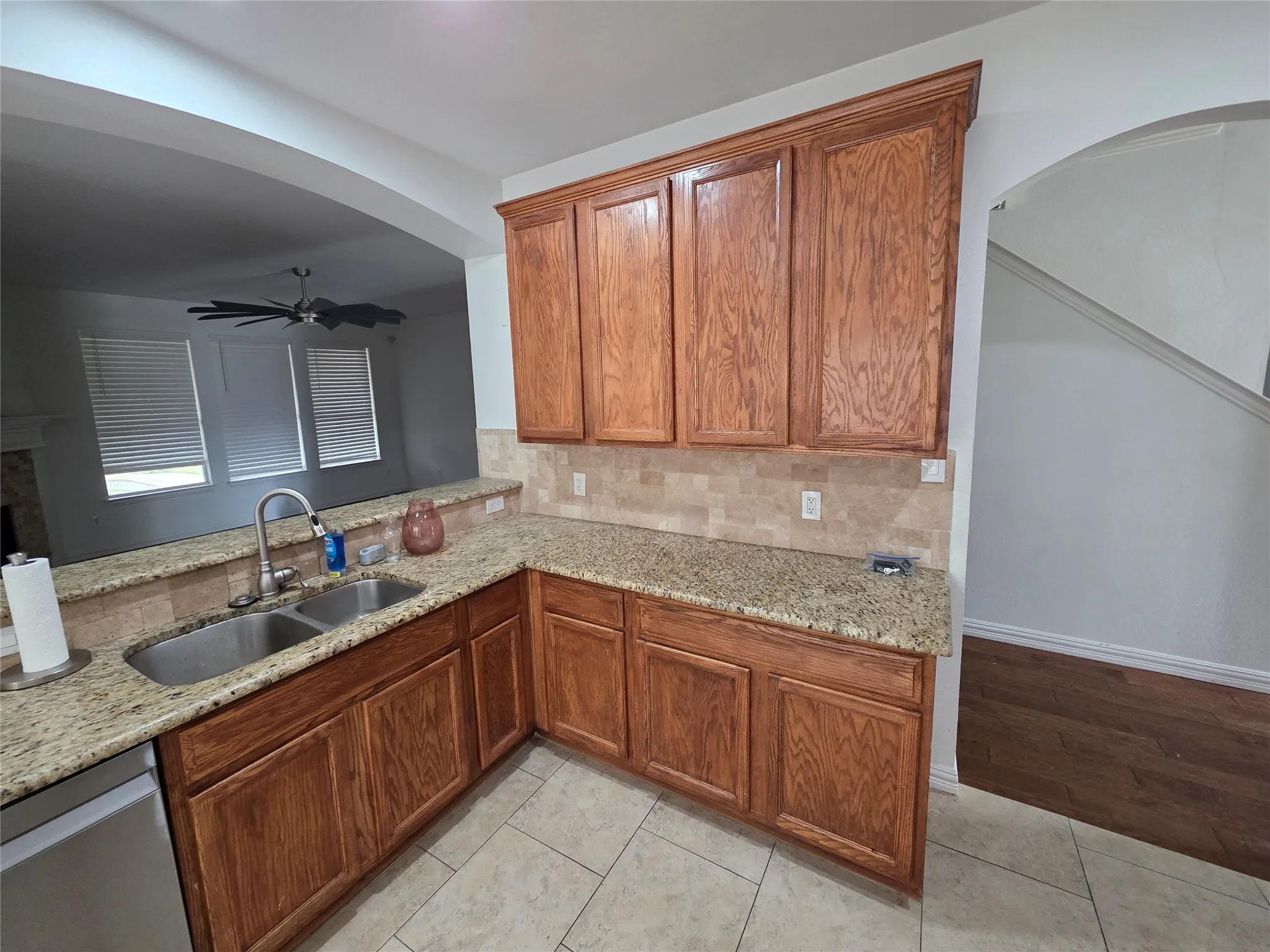 Kitchen featuring wood cabinetry, light-toned countertops, a stainless steel double basin sink with a gooseneck faucet, and a stone tile backsplash