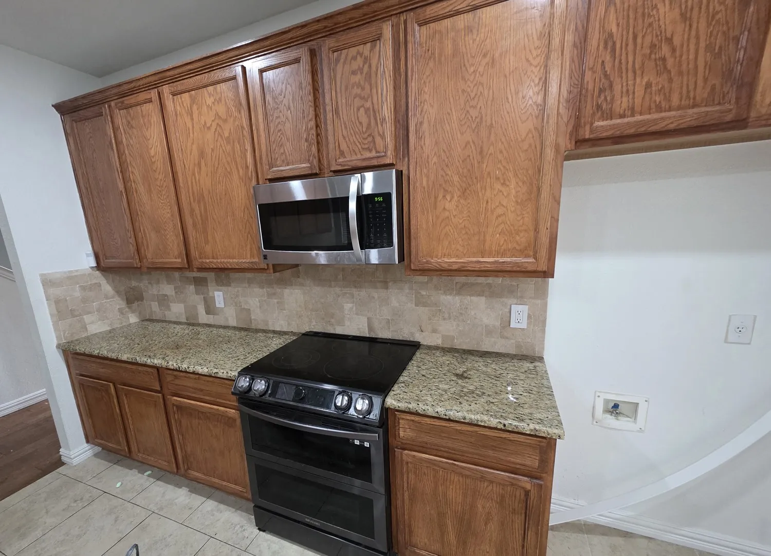 Kitchen featuring wood cabinetry, stone countertops, a tile backsplash, stainless steel microwave, and a black electric range