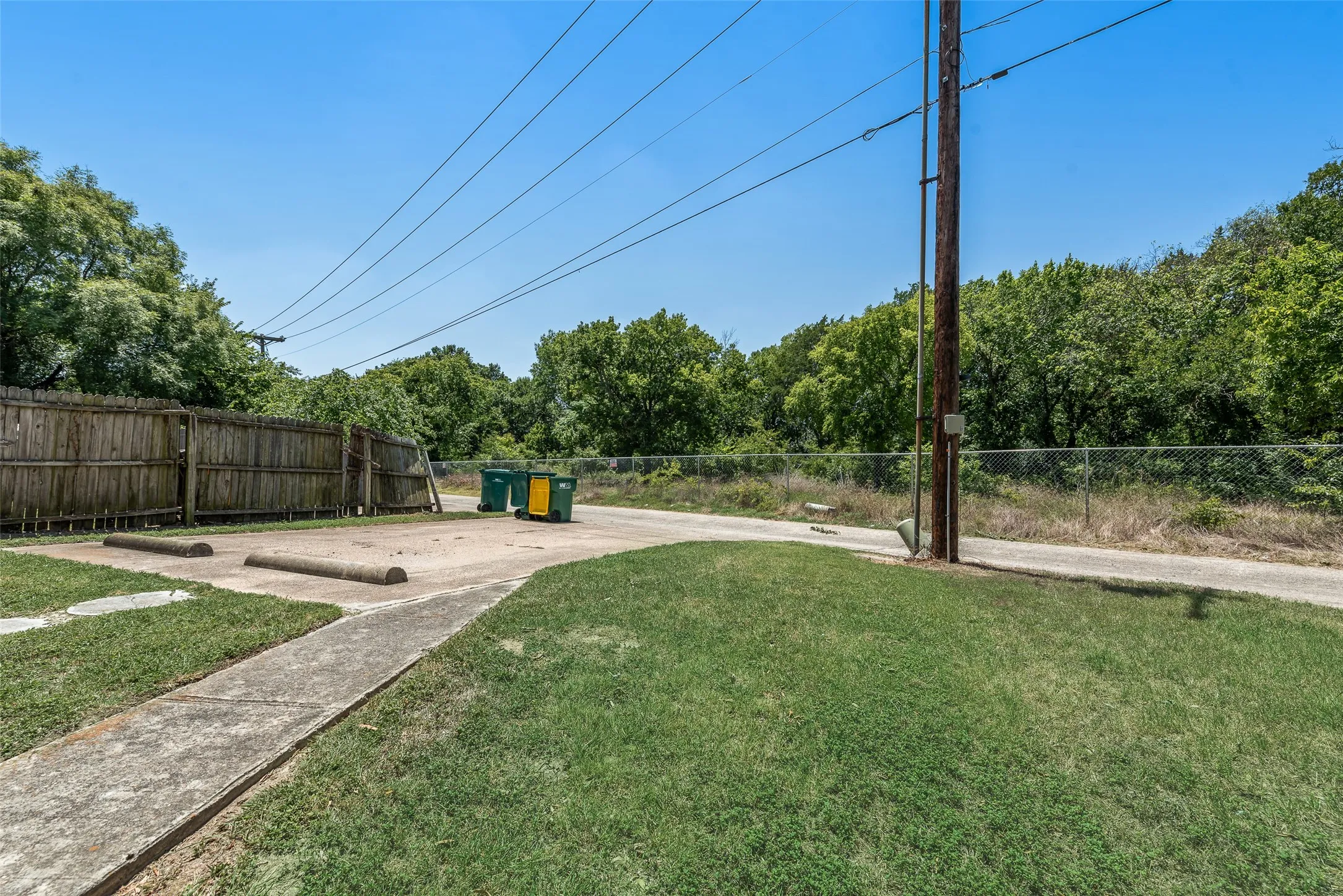 Paved parking area with concrete wheel stops, bordered by a wood privacy fence and chain link fence