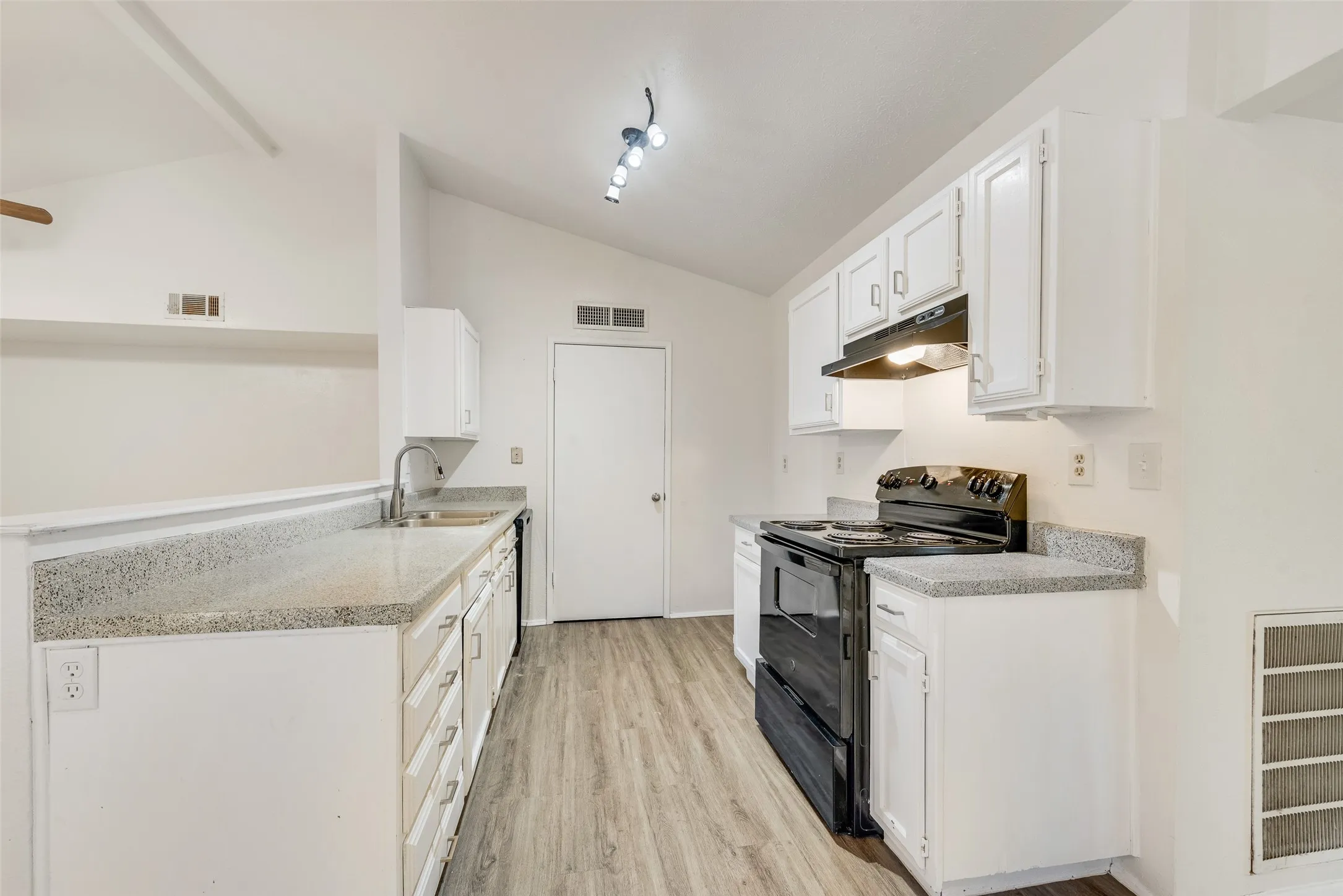 Kitchen featuring vaulted ceilings, wood-finish flooring, white cabinetry, speckled countertops, and a black electric range with a coordinating hood