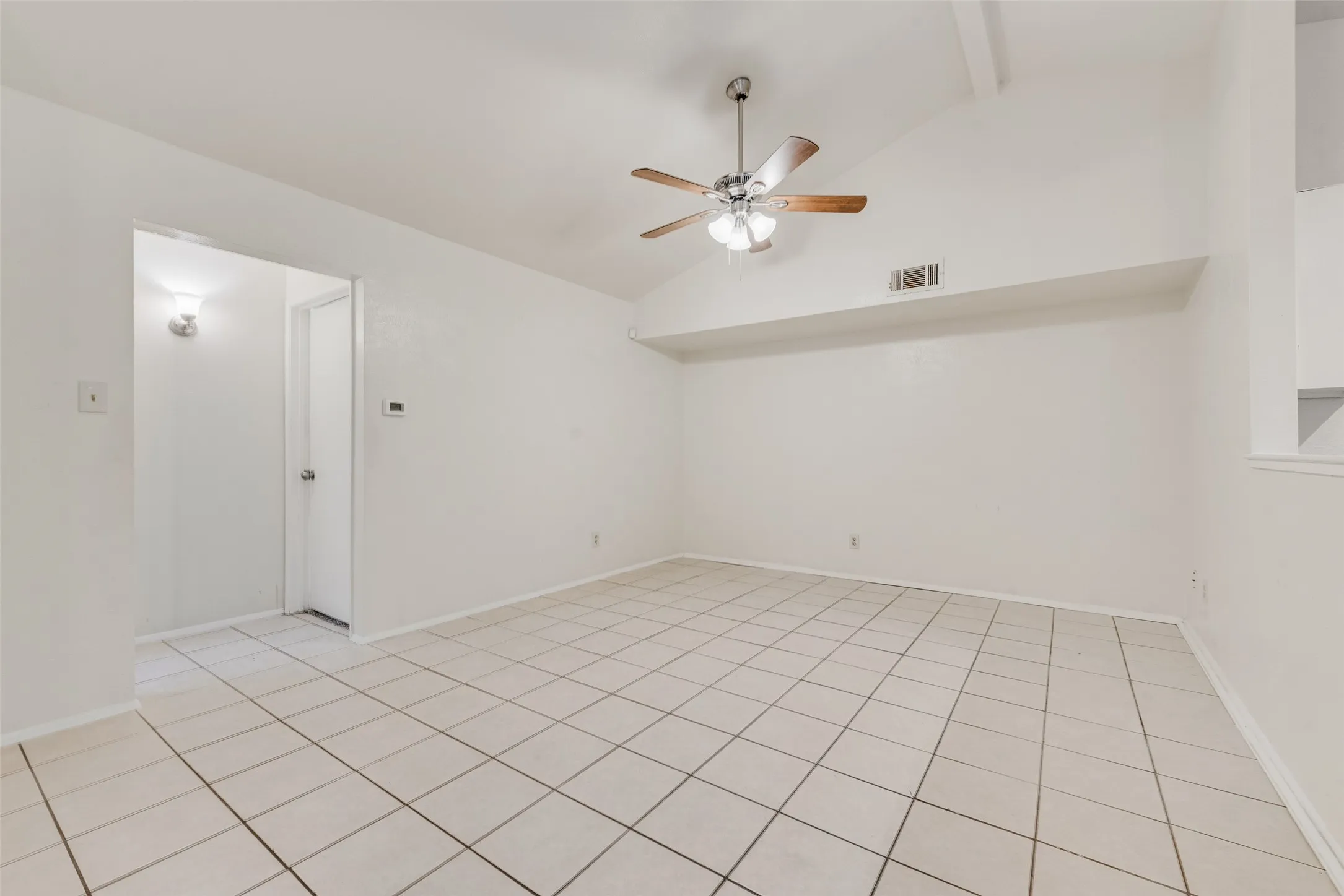 Spacious room featuring vaulted ceilings with exposed beams, a ceiling fan with light fixture, and tile flooring
