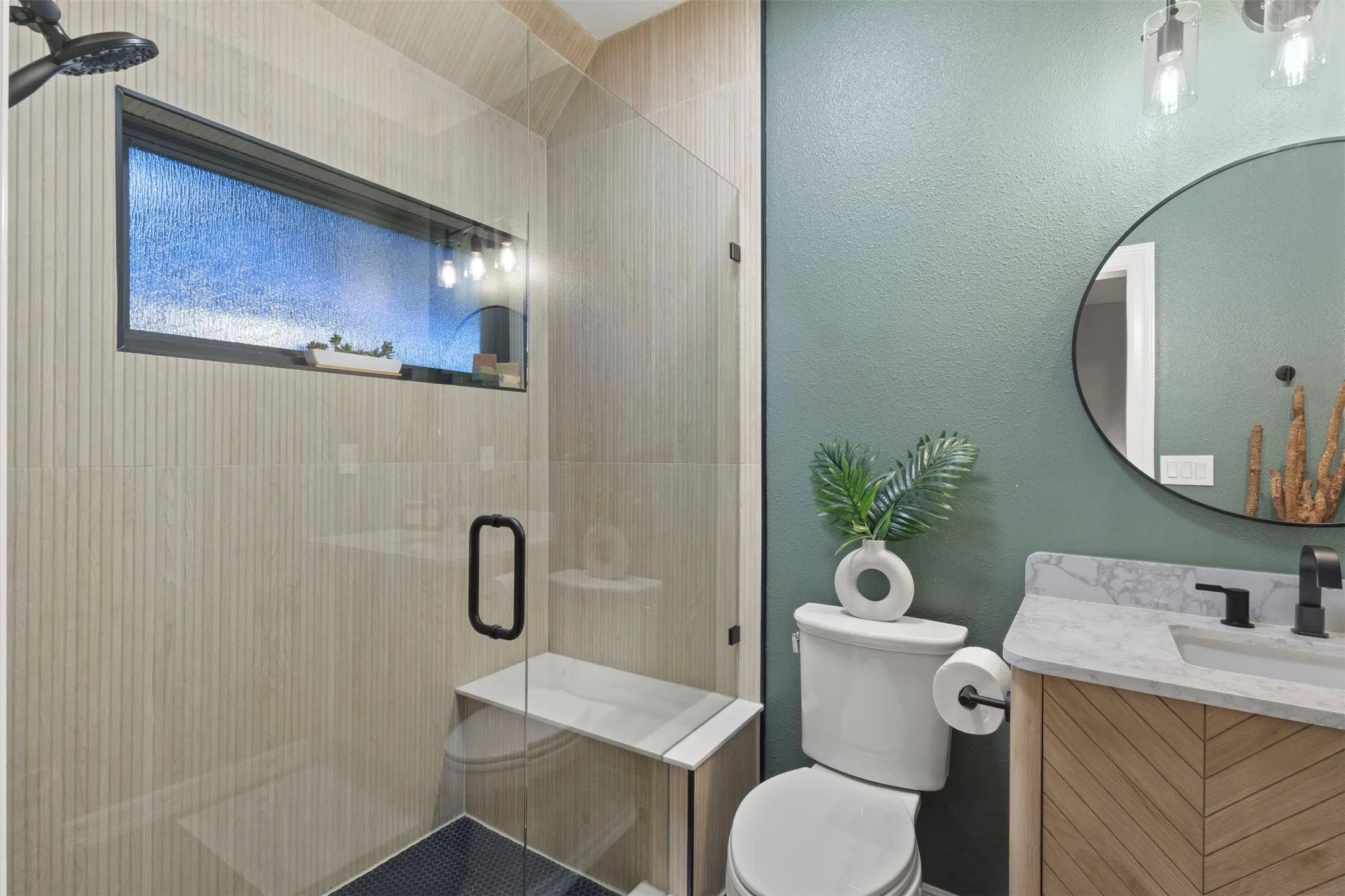Luxury guest ensuite bathroom fully remodeled with a custom bamboo glass window, floor-to-ceiling ribbon maple shower tile, basalt black stone flooring, large custom glass walk-in shower, quartz curb and bench, and updated vanity with quartz countertop, new lighting, and toilet.