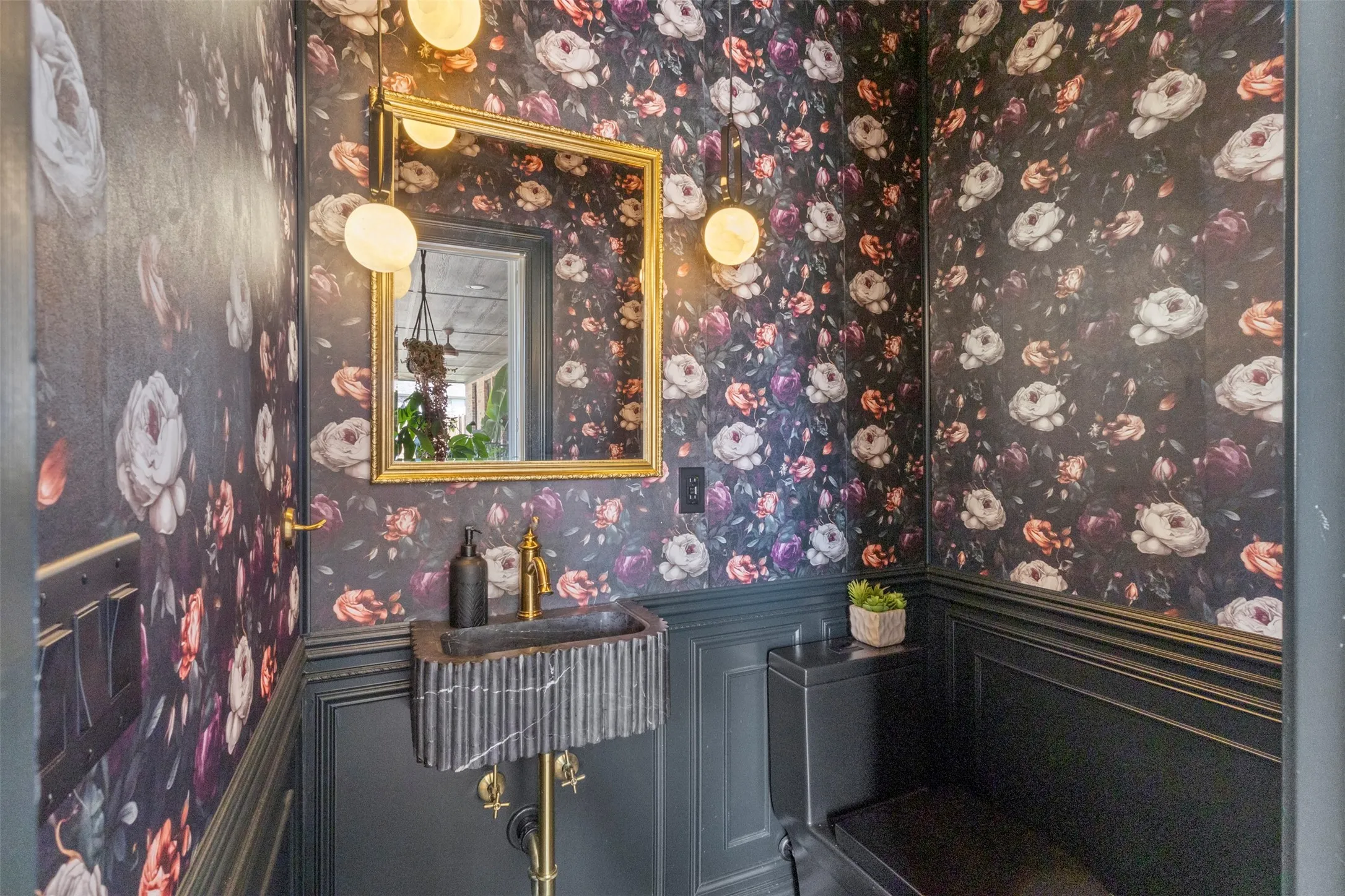 Dramatic powder bath featuring black basalt marble herringbone tile extending to the ceiling at the sink, rich floral wallcovering, black wainscoting, and statement lighting—creating a bold, jewel-box luxury finish.