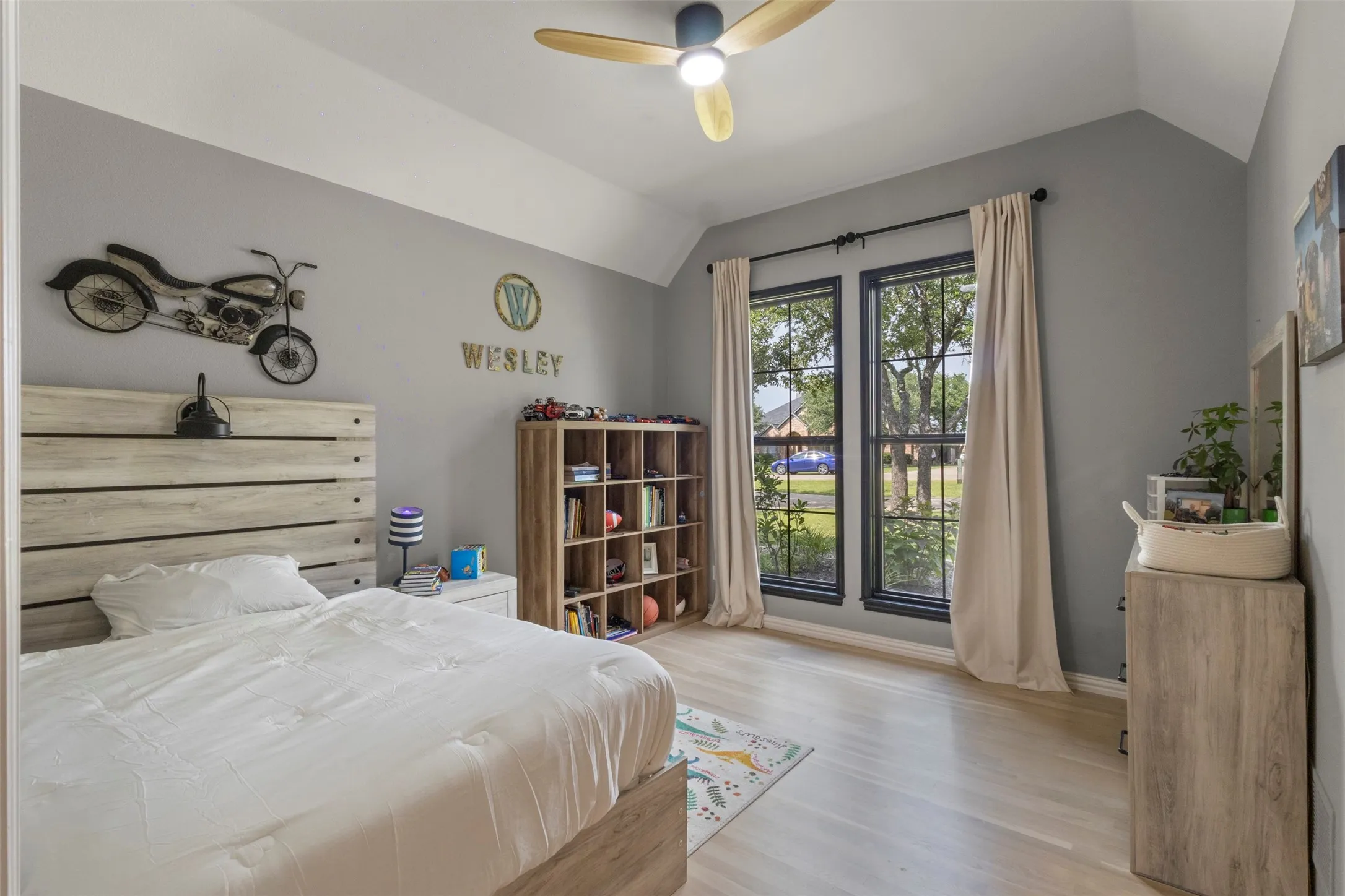Bright secondary bedroom featuring vaulted ceilings, large windows, updated trim details, and replaced white oak hardwood flooring—creating a fresh, elevated space with natural light and timeless designer appeal.