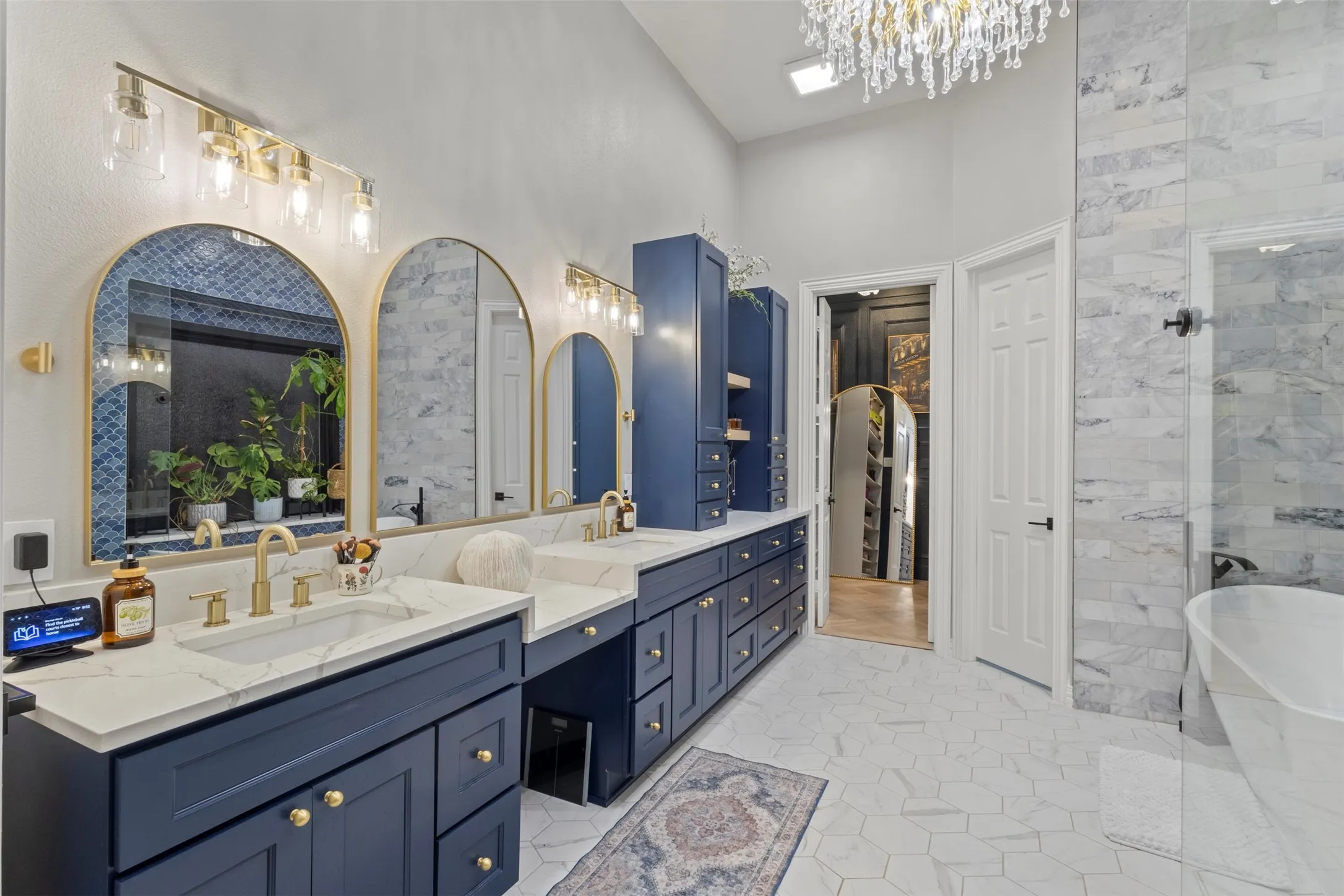 Spa-inspired primary bathroom fully renovated with 12’ ceilings, floor-to-ceiling tile, a custom frameless glass shower, standalone soaking tub, Calacatta quartz countertops, and 16’ of Sherwin-Williams Naval custom cabinetry with gold hardware and a statement teardrop glass chandelier.