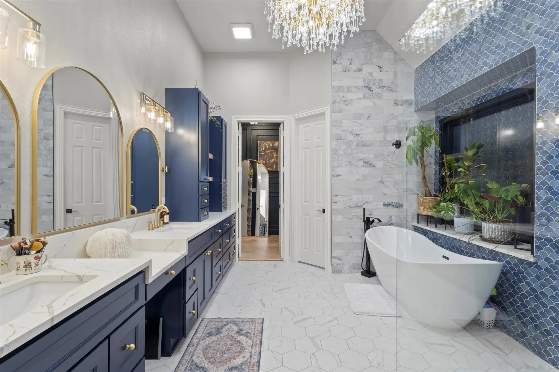 Spa-inspired primary bathroom fully renovated with 12’ ceilings, floor-to-ceiling tile, a custom frameless glass shower, standalone soaking tub, Calacatta quartz countertops, and 16’ of Sherwin-Williams Naval custom cabinetry with gold hardware and a statement teardrop glass chandelier.