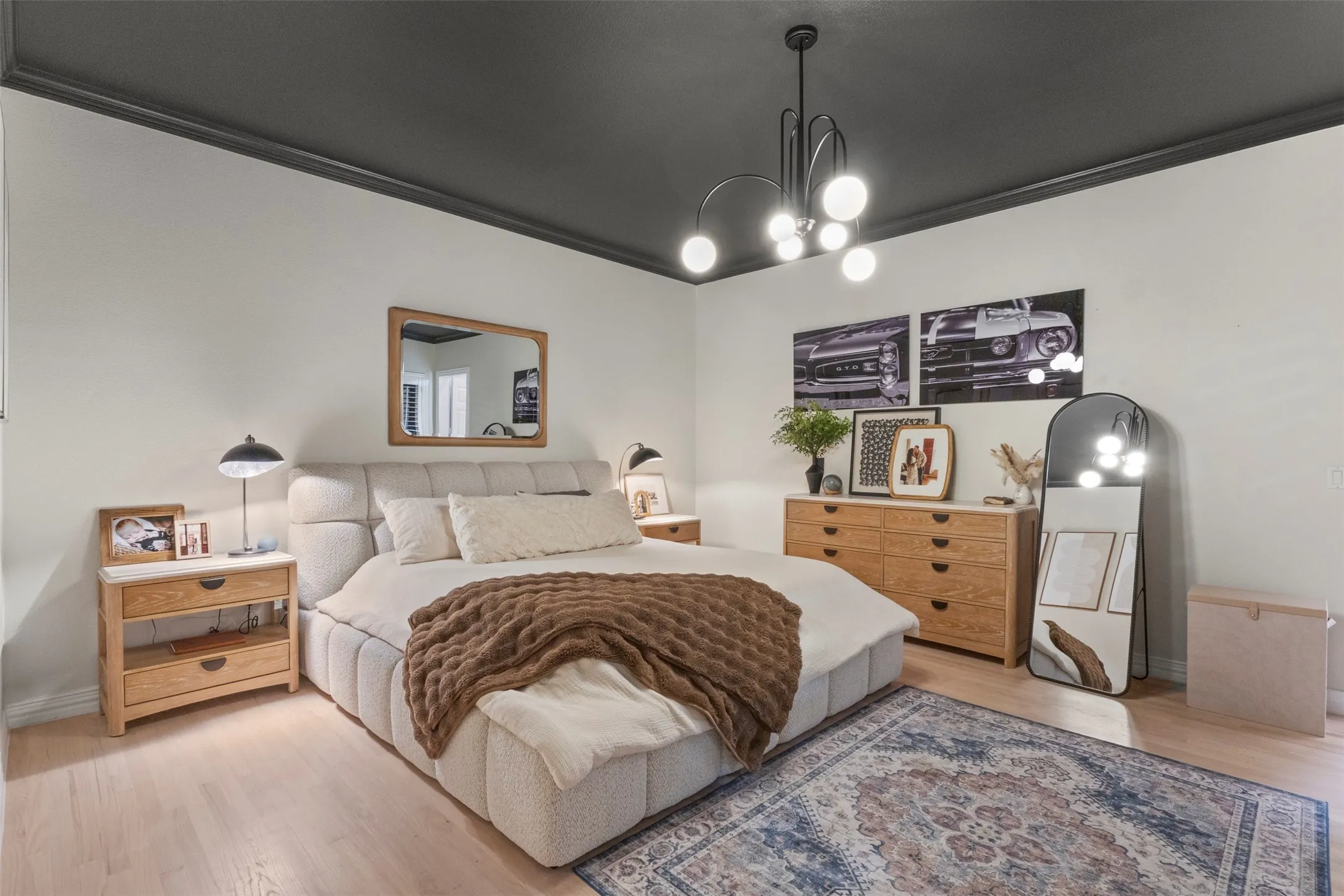 Designer bedroom retreat featuring white oak flooring, a dramatic dark ceiling with matching crown molding, modern statement lighting, and warm natural wood furnishings—creating a sophisticated, elevated space with a boutique-luxury feel.