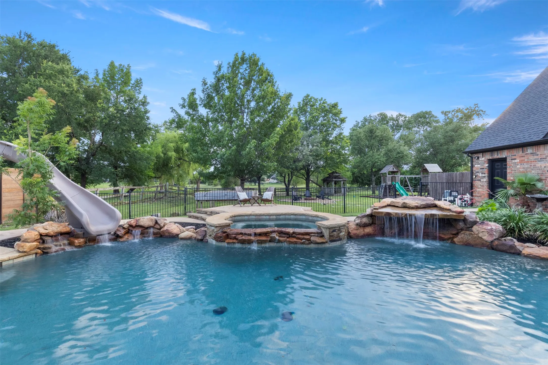 Resort-style backyard featuring a saltwater pool with updated heater, pumps, and waterfall motor, plus a rock waterfall, spa, and slide—creating a private outdoor retreat designed for luxury entertaining and relaxation.