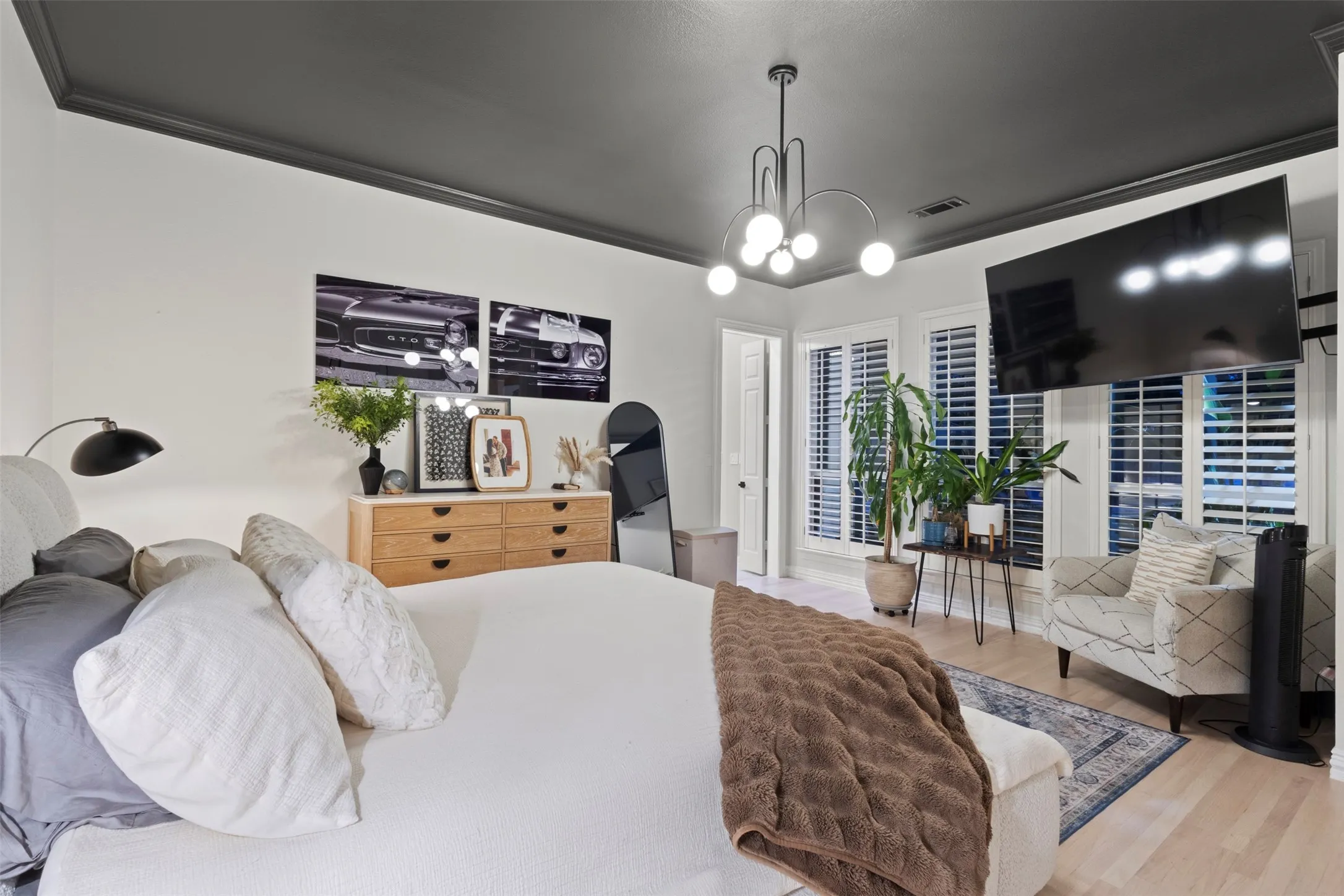 Designer bedroom retreat featuring white oak flooring, a dramatic dark ceiling with matching crown molding, modern statement lighting, and warm natural wood furnishings—creating a sophisticated, elevated space with a boutique-luxury feel.