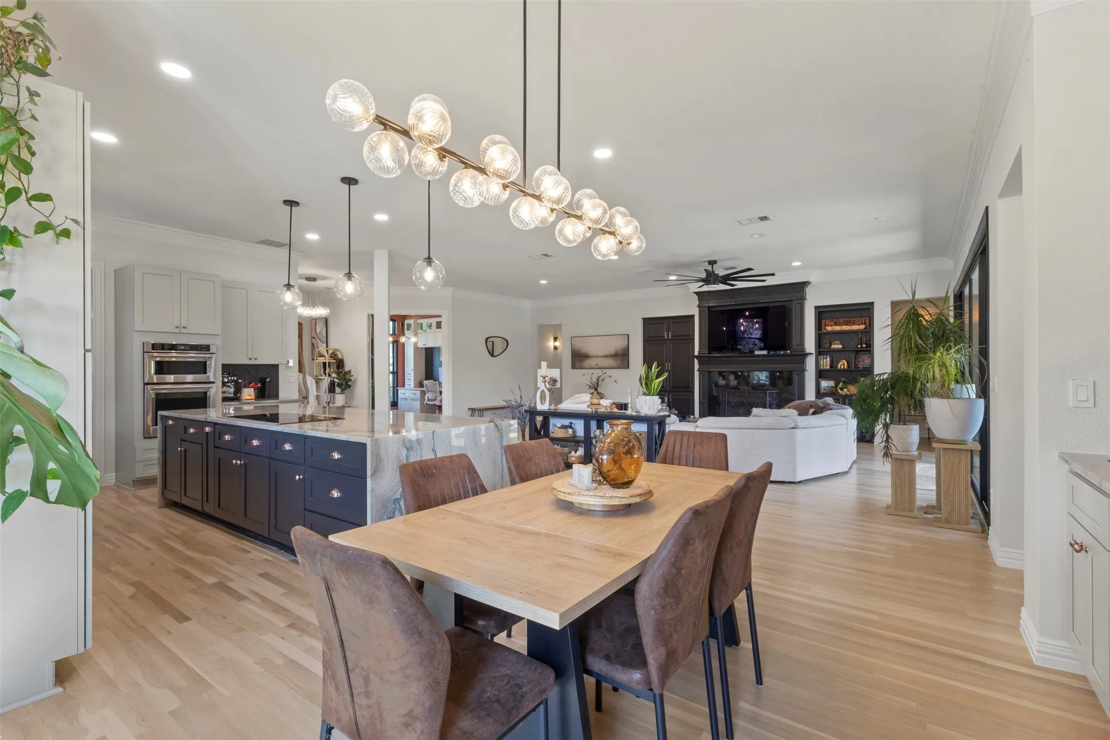 Elegant eat-in kitchen featuring statement designer lighting, white oak flooring, custom cabinetry, and striking Aquarela quartzite countertops—seamlessly connected to the living area for elevated everyday dining and luxury entertaining.