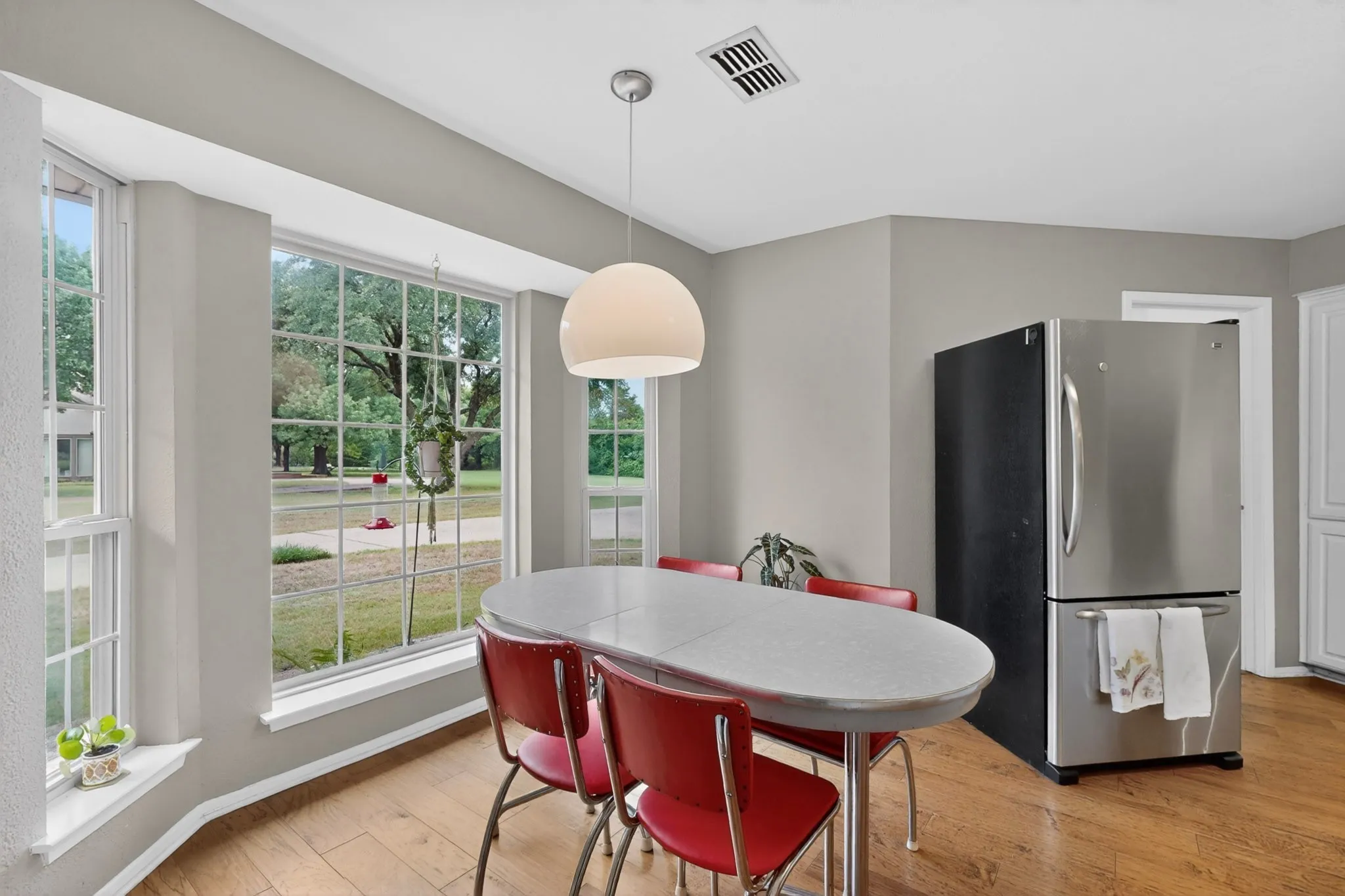 Bay window with multiple panes, wood-finish flooring, a contemporary pendant light fixture, a stainless steel refrigerator, and light grey wall paint