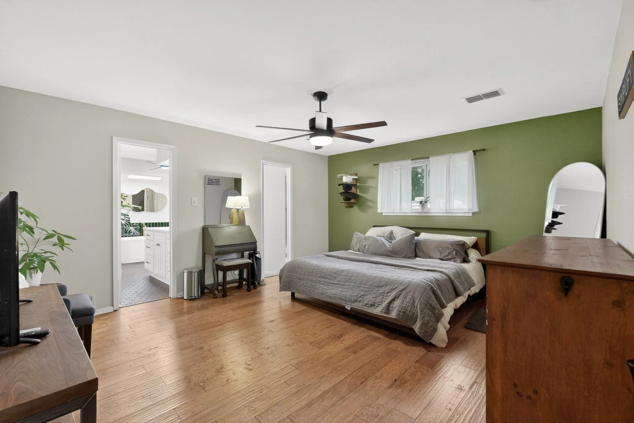 Spacious bedroom featuring wood-finish flooring, a ceiling fan with integrated lighting, and a window with natural light