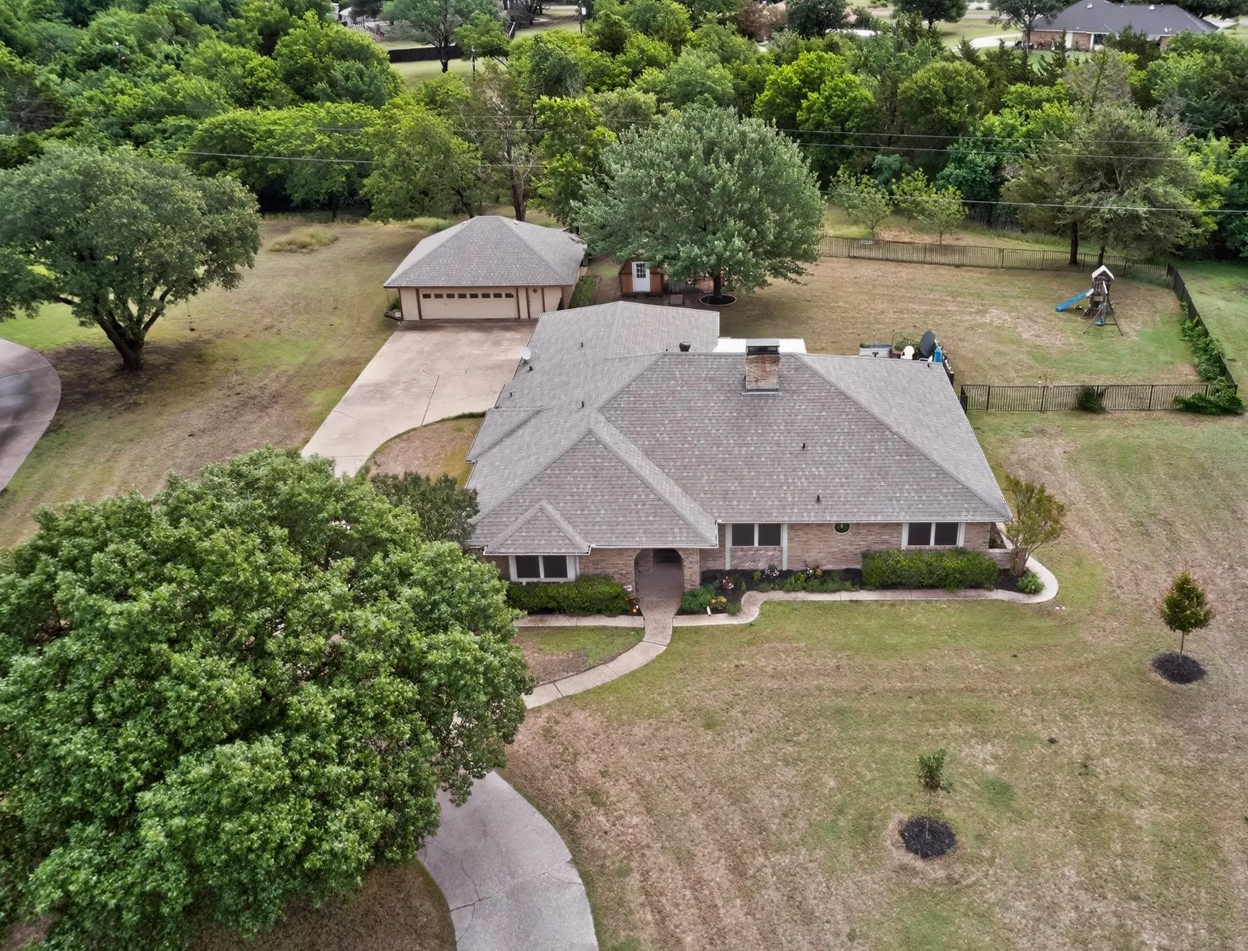 Brick residence with a shingle roof, featuring a detached garage, concrete driveway, and established trees