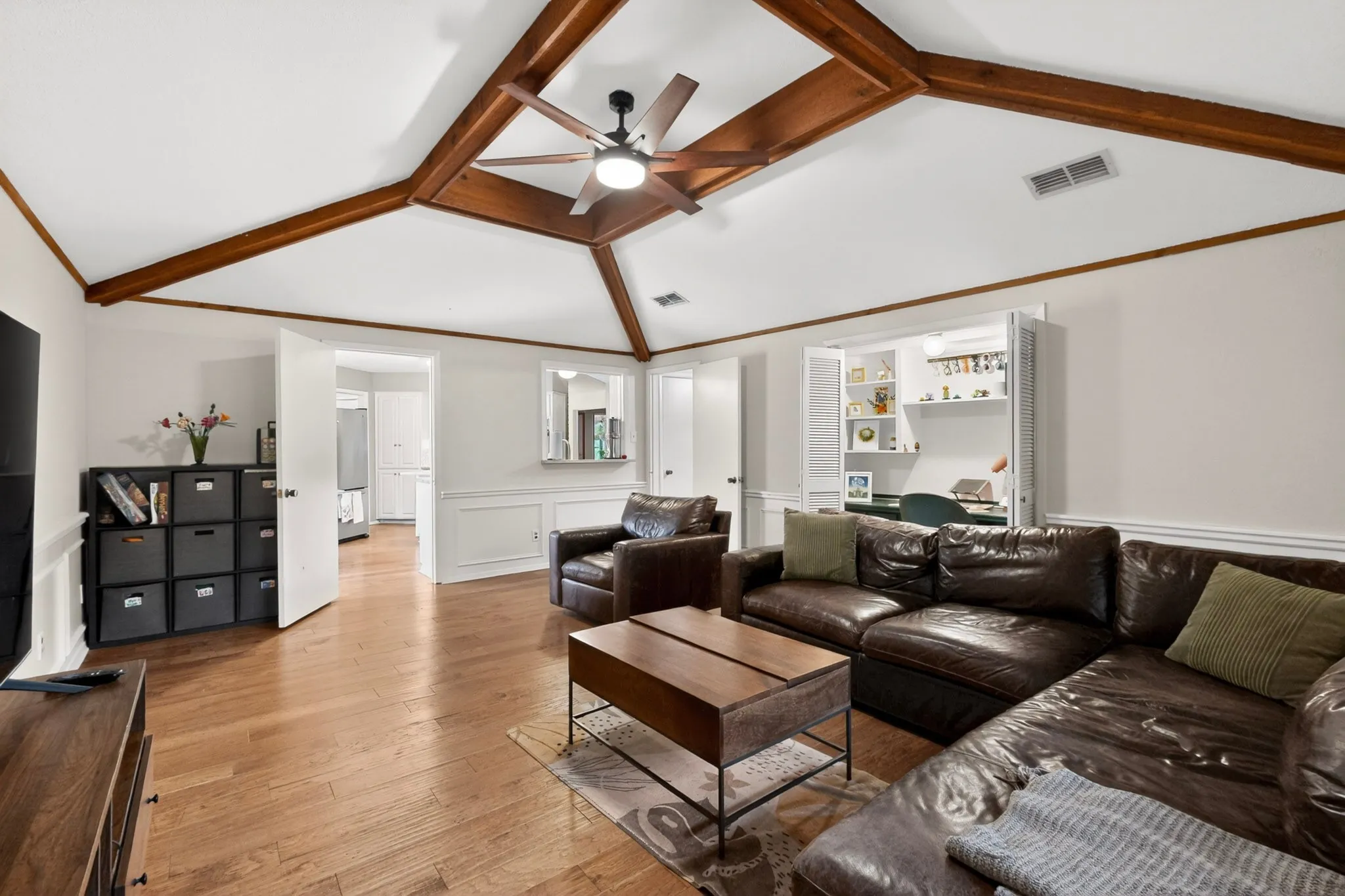 Living area featuring vaulted ceilings with exposed wood beams, wood-finish flooring, wainscoting, and a built-in desk with shelving