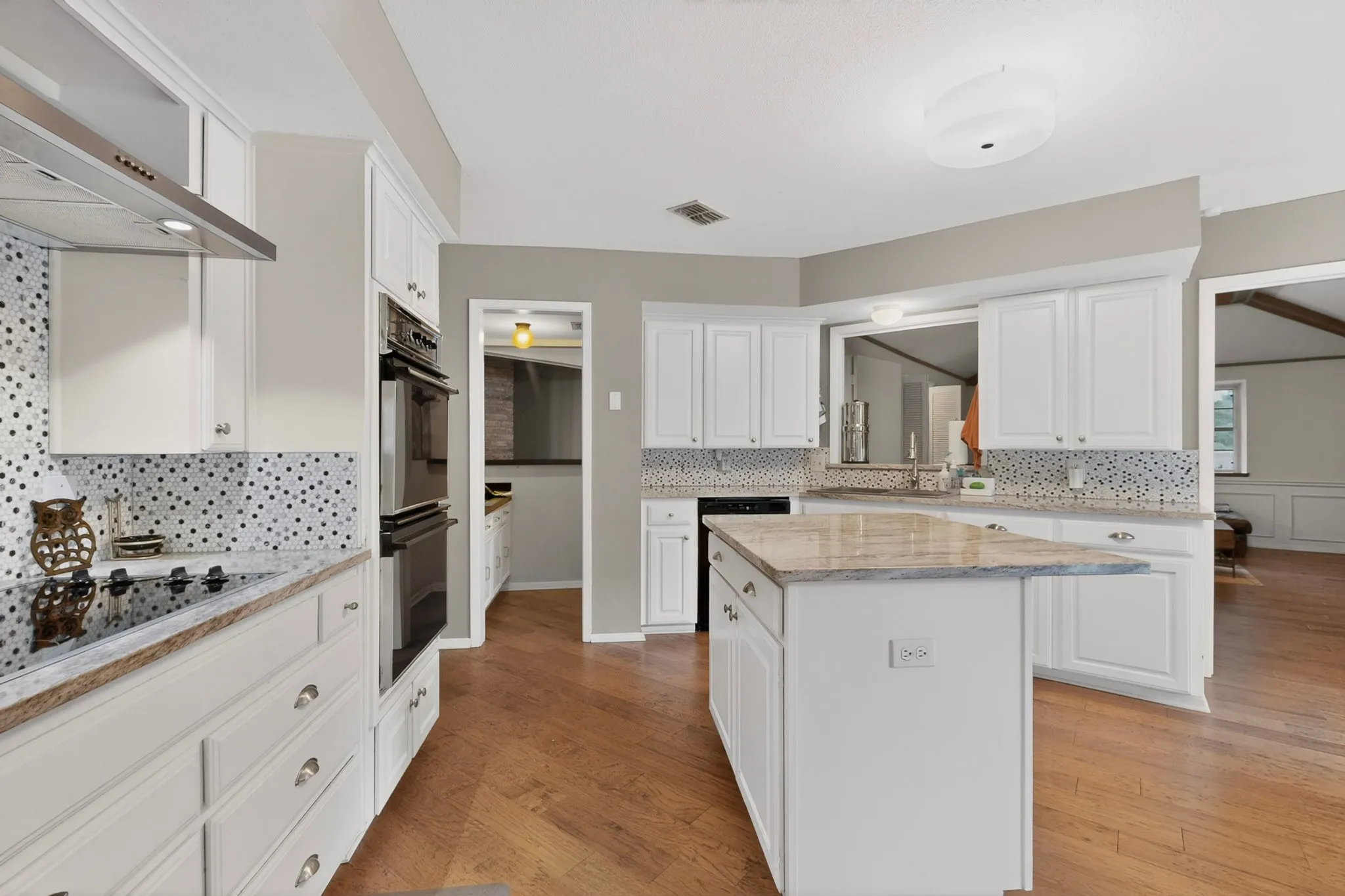 Modern kitchen featuring white cabinetry, granite countertops, a built-in double oven, a smooth cooktop, and a mosaic tile backsplash
