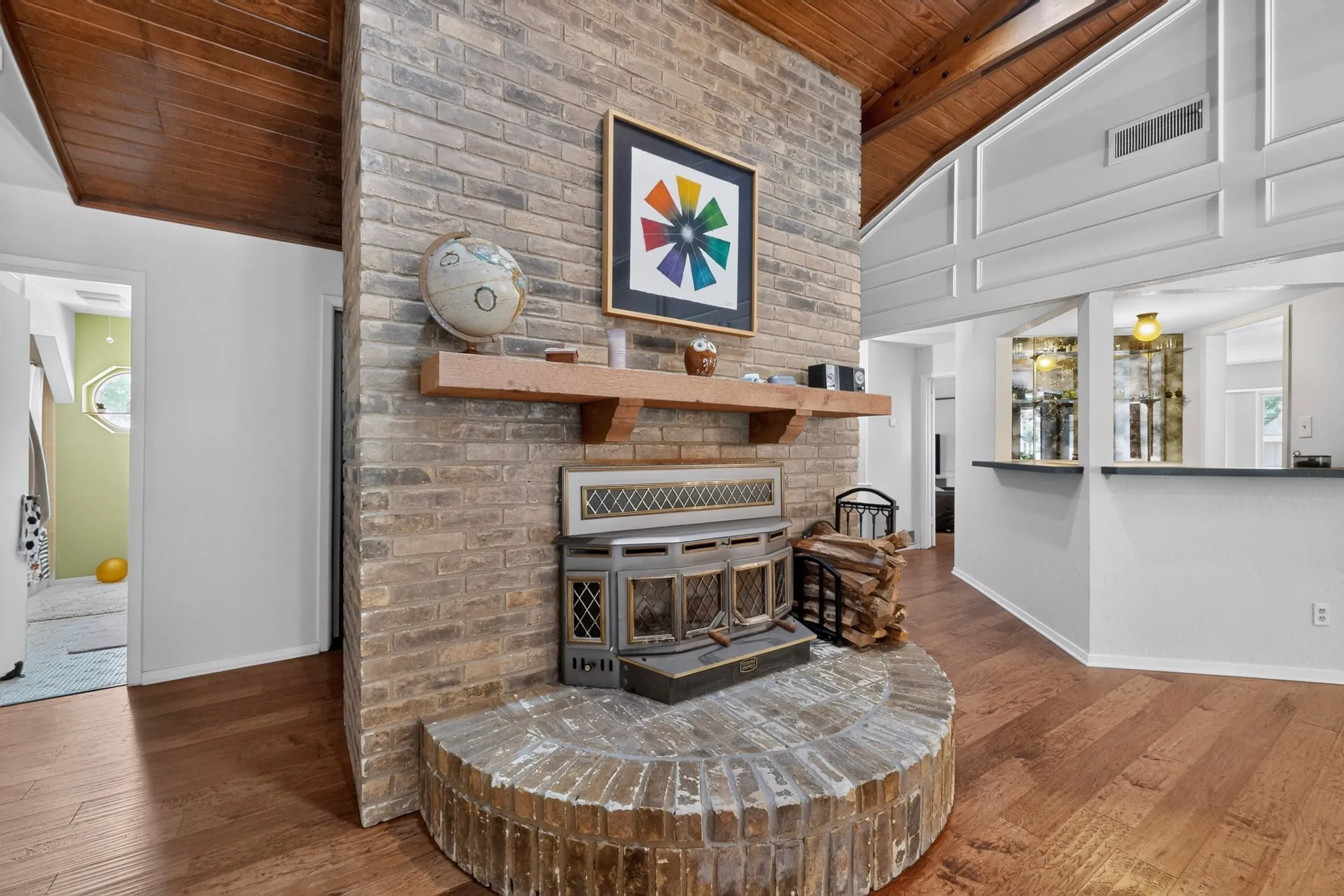 Brick fireplace with a wood mantel, wood-finish flooring, and a vaulted wood-paneled ceiling