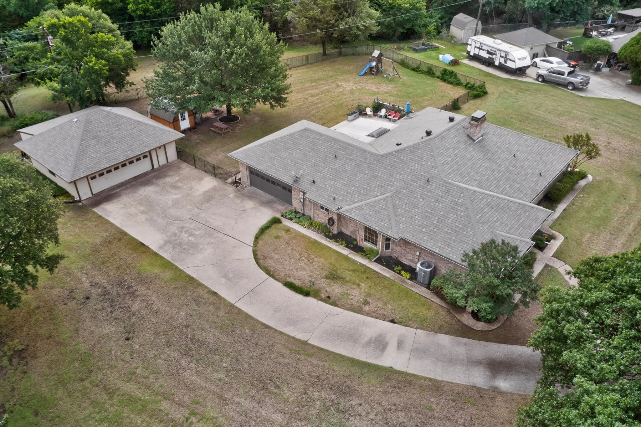 Expansive property featuring a main residence with a multi-level roofline, a detached garage, a concrete driveway, a paved patio area, and mature landscaping