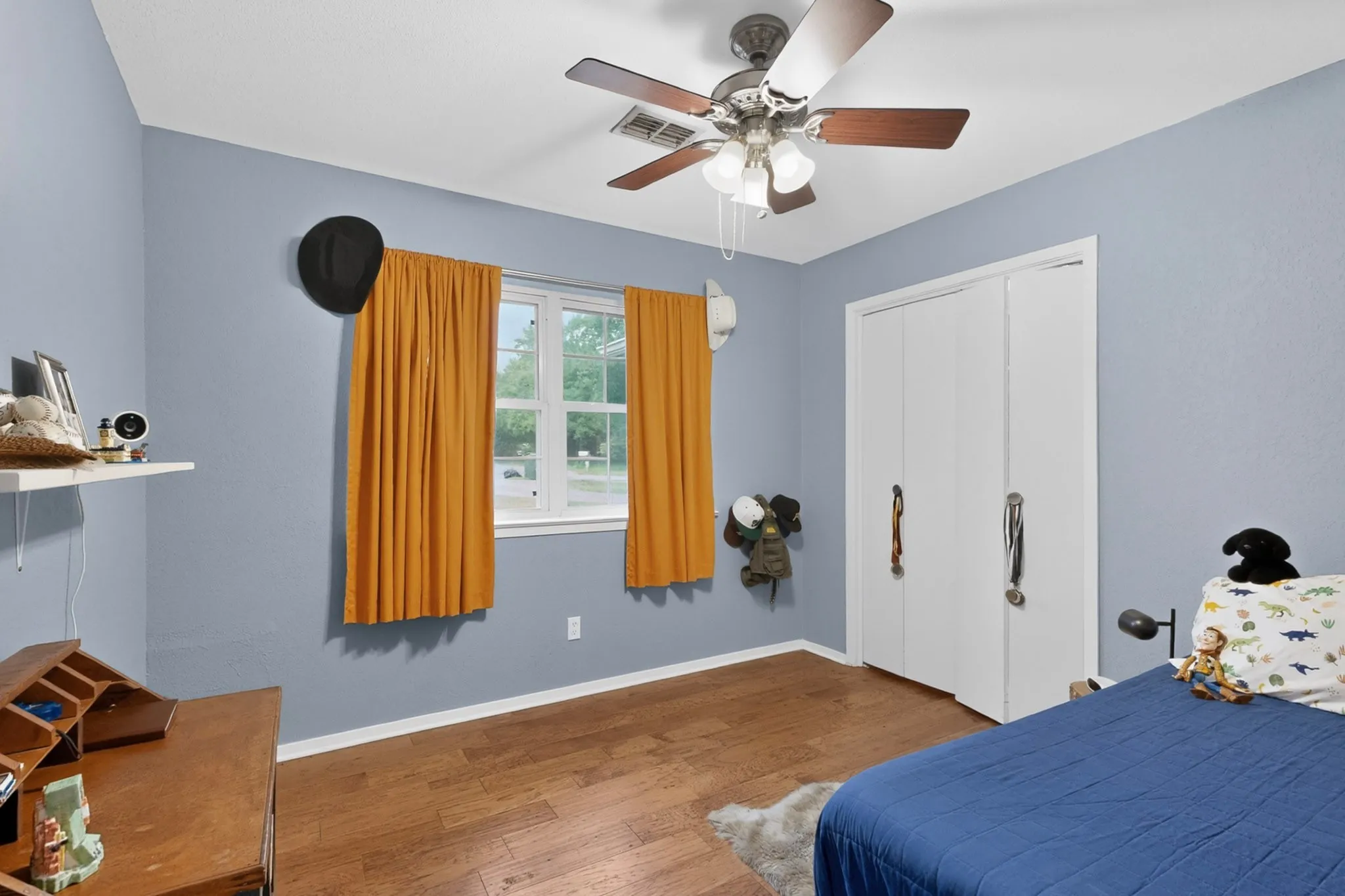 Bedroom featuring wood-finish flooring, a ceiling fan with light fixture, and a window with white trim