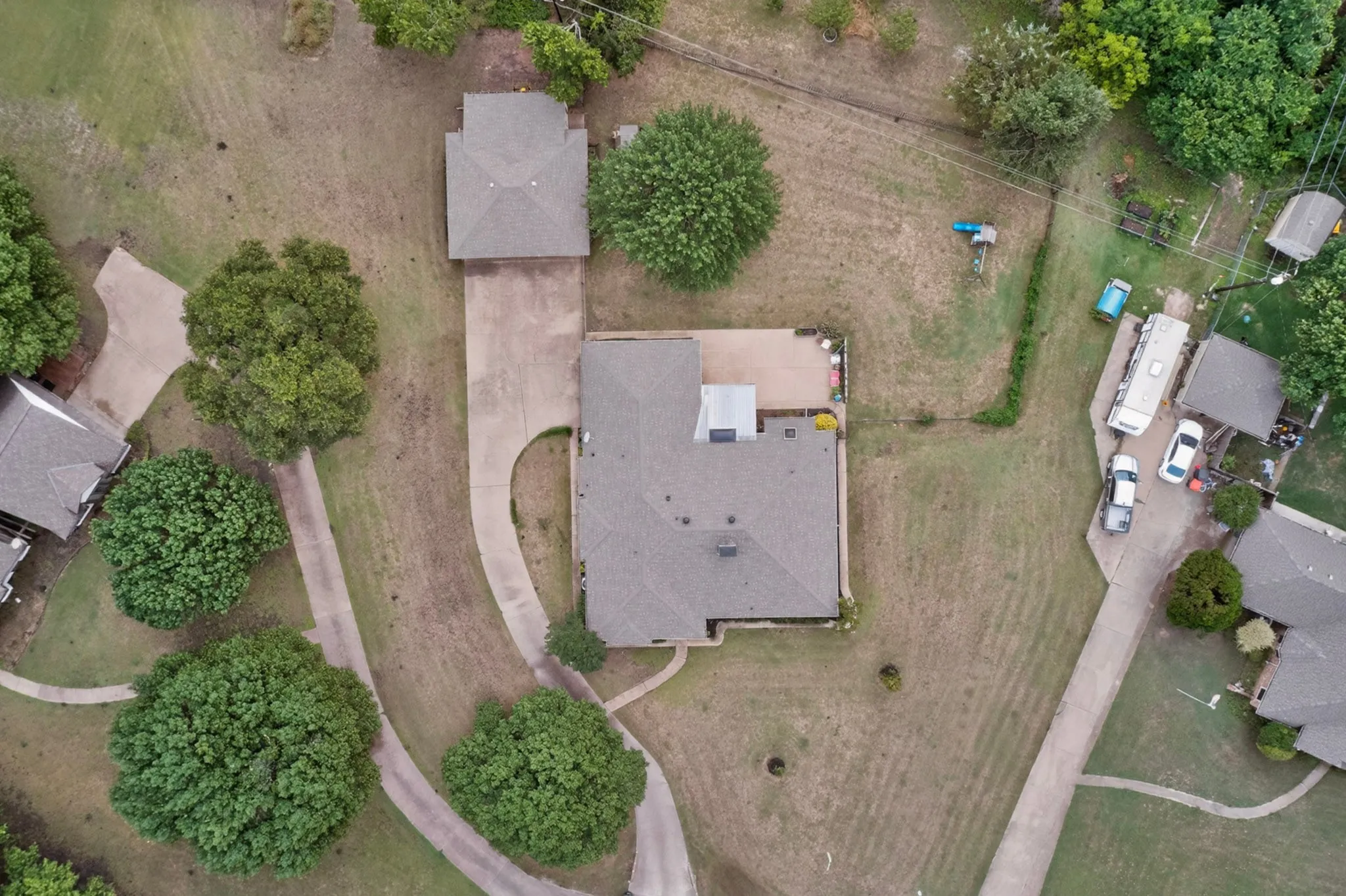 Expansive property featuring a main residence with an additional detached structure, mature trees, and concrete driveways