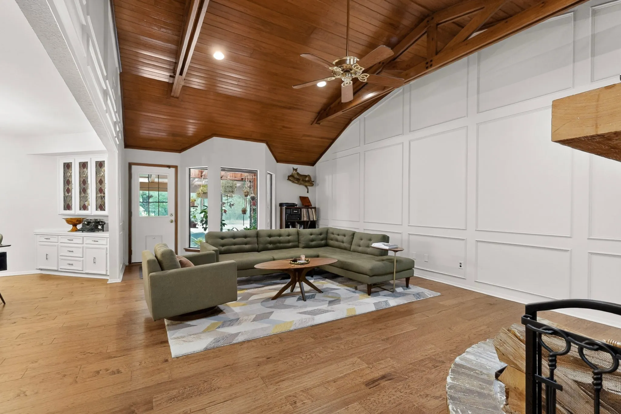 Vaulted wood-finish ceiling with exposed beams, wood-finish flooring, white paneled accent wall, built-in white cabinetry, and multi-pane windows