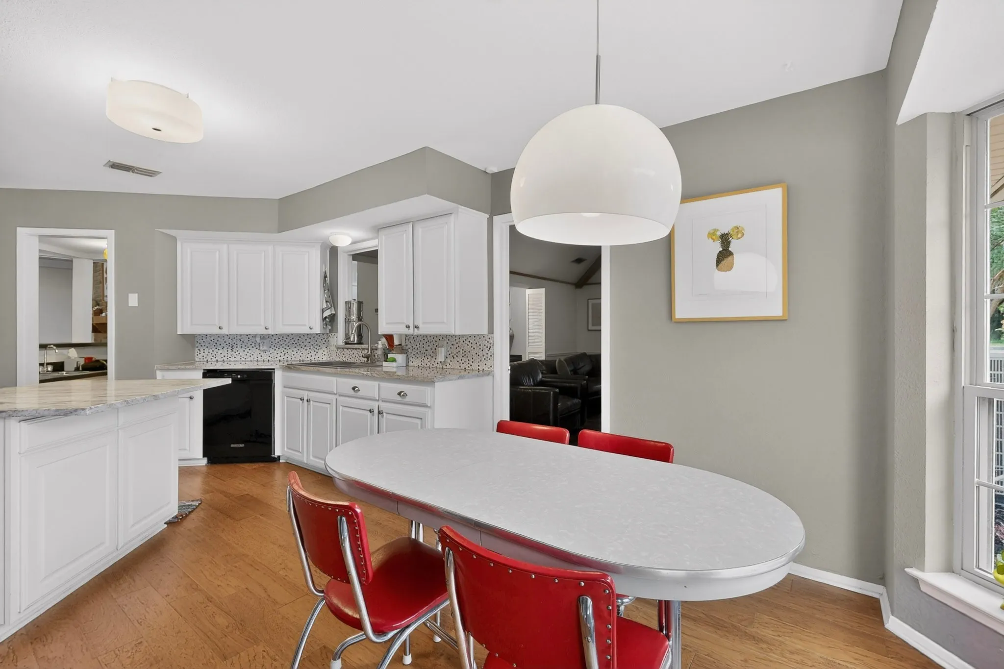 Bright kitchen featuring white cabinetry, light-toned countertops, a mosaic tile backsplash, wood-finish flooring, and a contemporary pendant light fixture