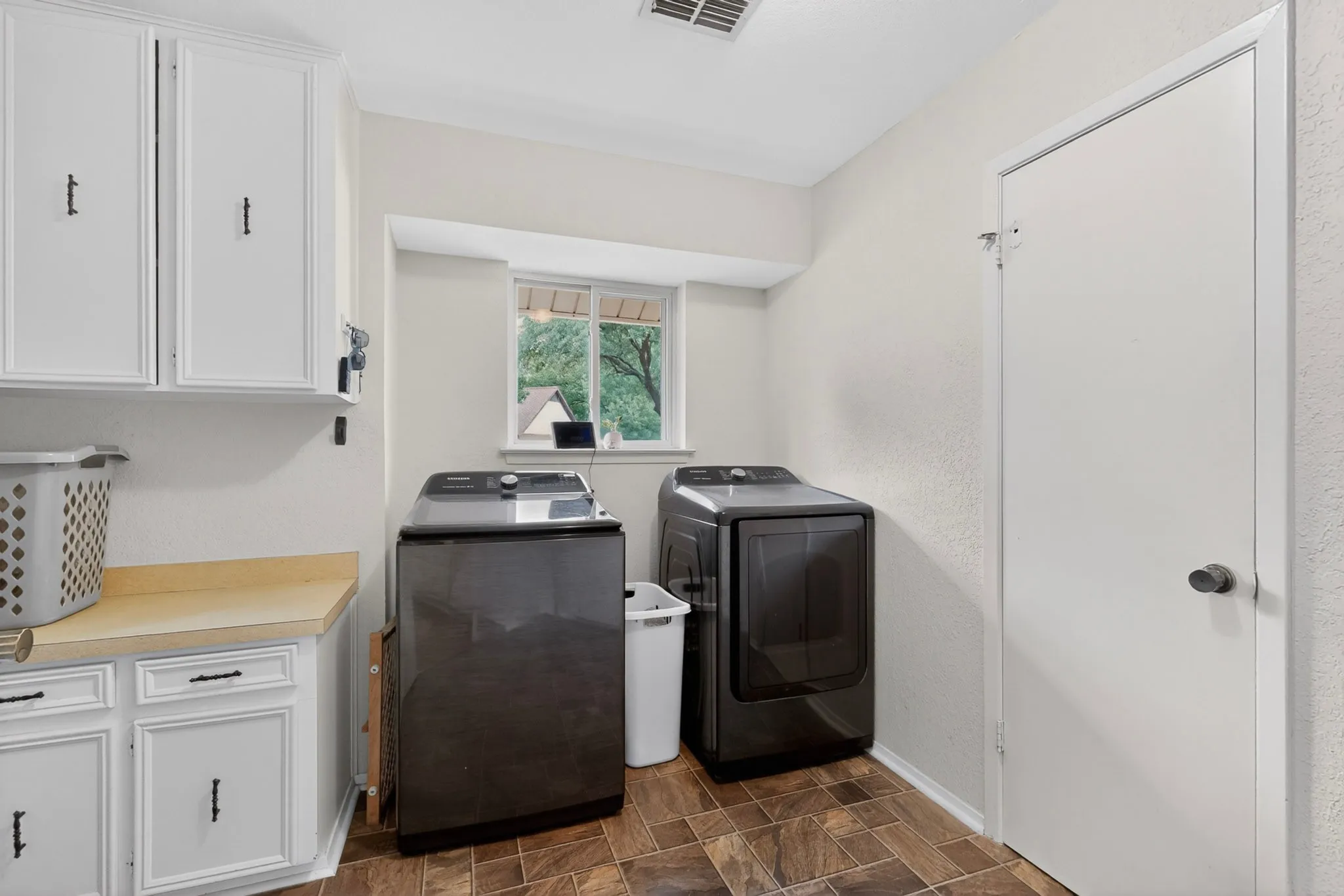 Functional utility room featuring white cabinetry with dark hardware, a light-toned countertop, a window, and tile flooring