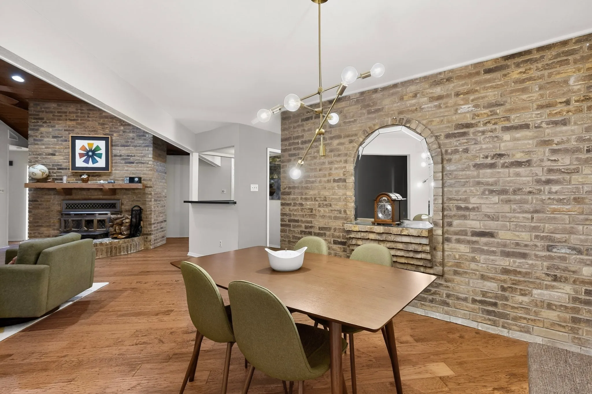 Dining area featuring a modern linear chandelier, a brick accent wall with an arched opening, and wood-finish flooring