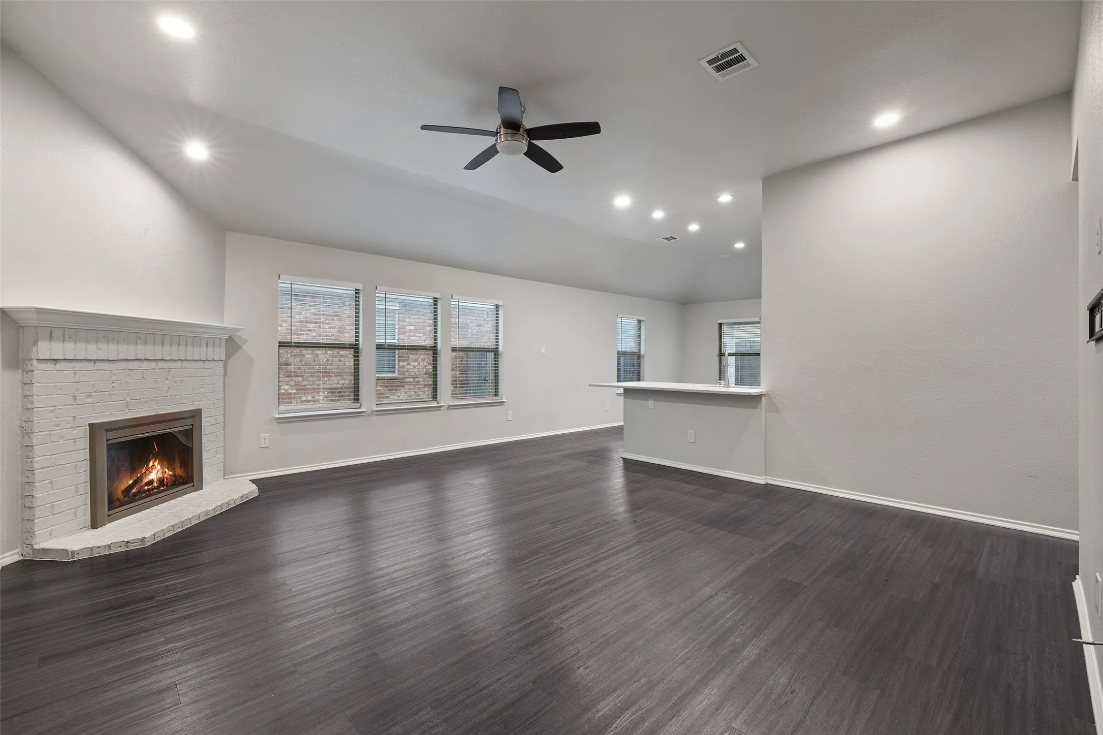 Unfurnished living room with dark hardwood / wood-style floors, ceiling fan, vaulted ceiling, and a fireplace