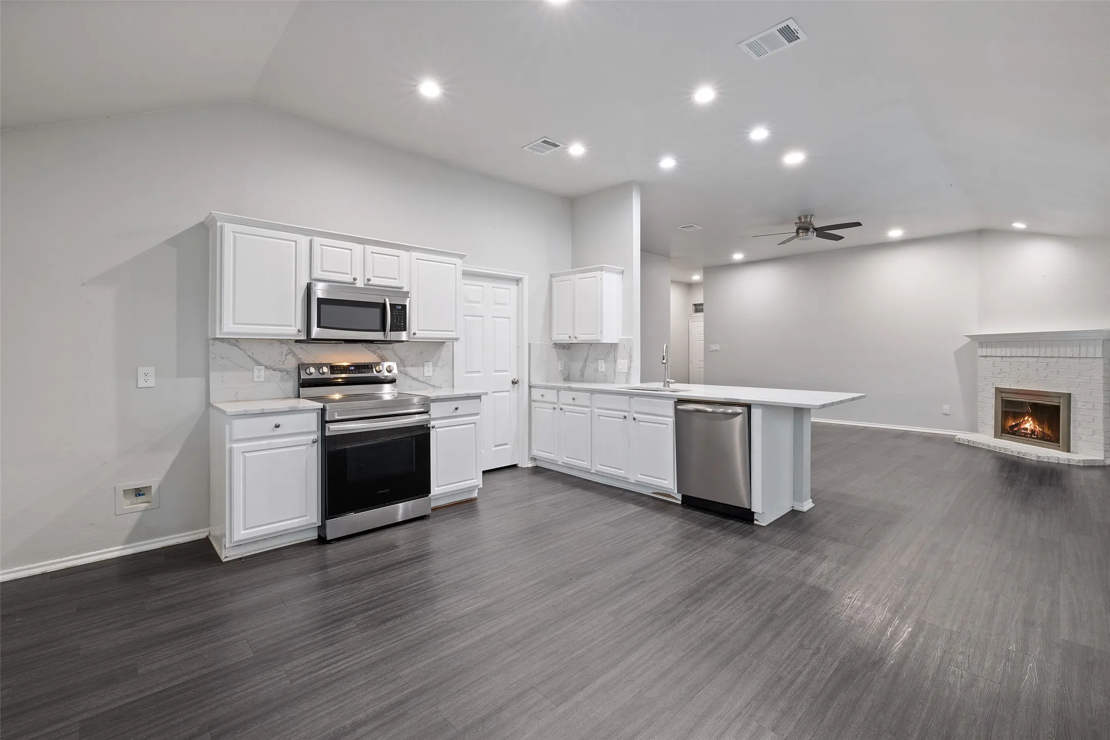 Kitchen featuring dark hardwood / wood-style flooring, appliances with stainless steel finishes, a brick fireplace, kitchen peninsula, and ceiling fan