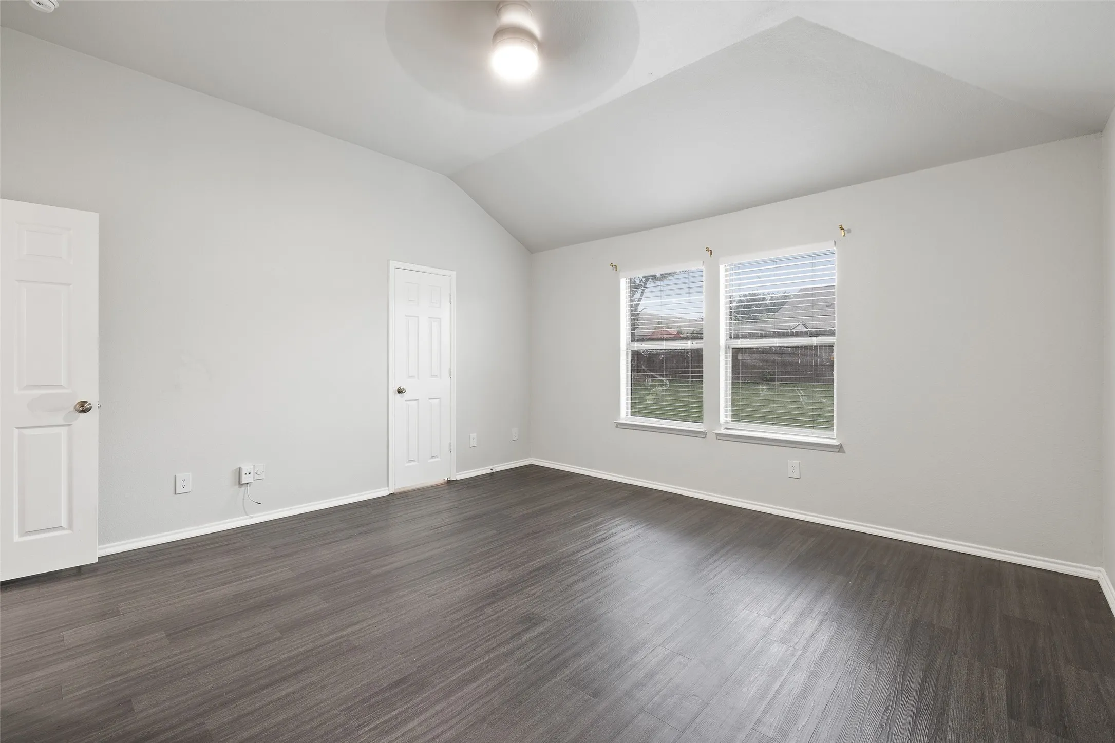 Empty room featuring ceiling fan, vaulted ceiling, and dark wood-type flooring