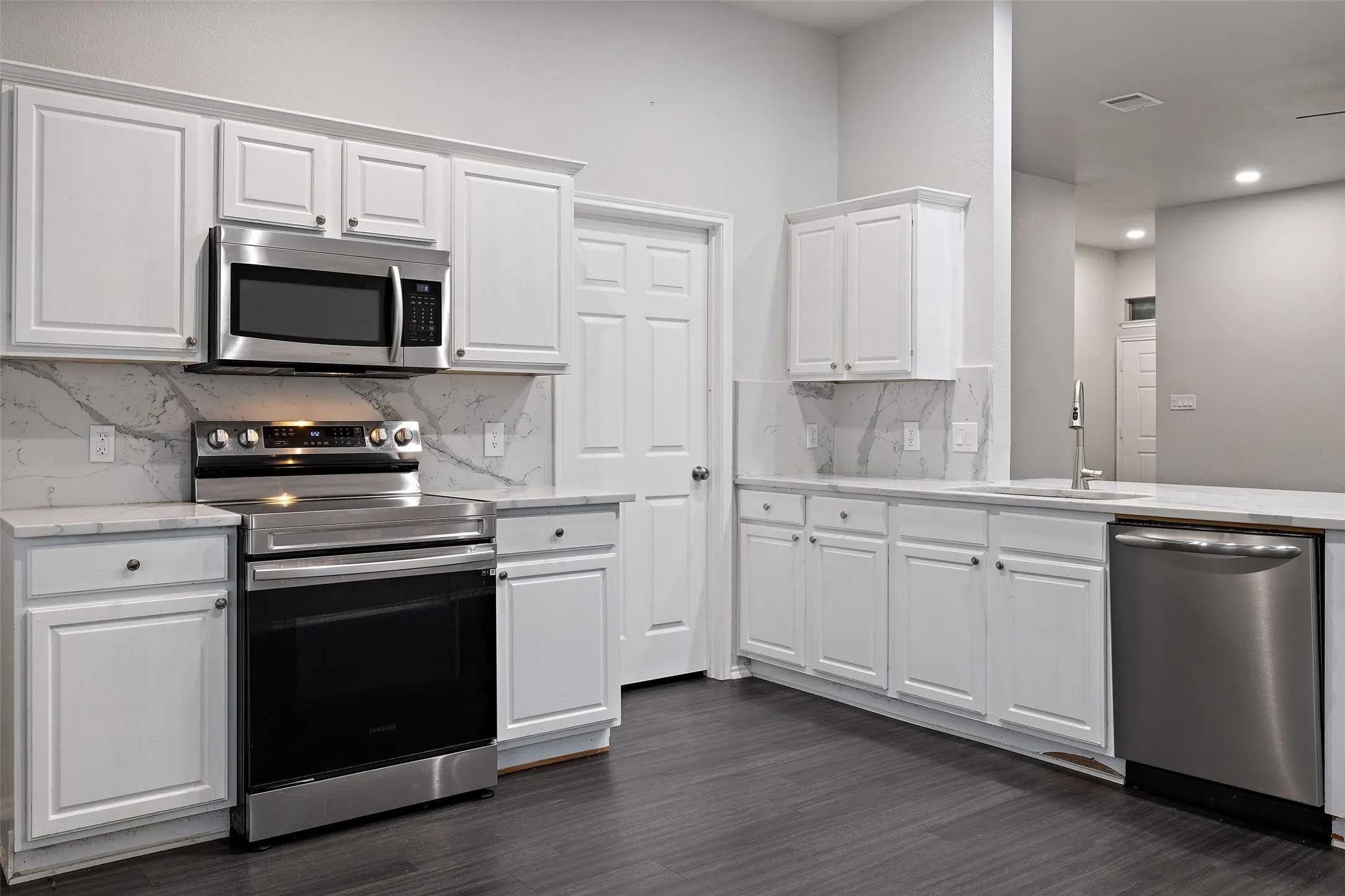 Kitchen with dark hardwood / wood-style floors, stainless steel appliances, tasteful backsplash, white cabinets, and sink