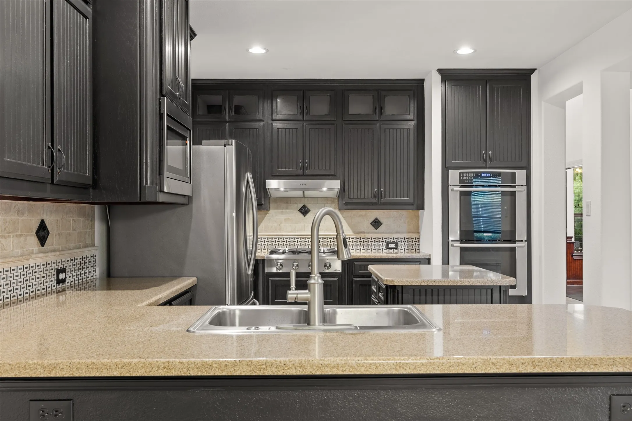 Kitchen with backsplash, double oven, sink, and light stone countertops