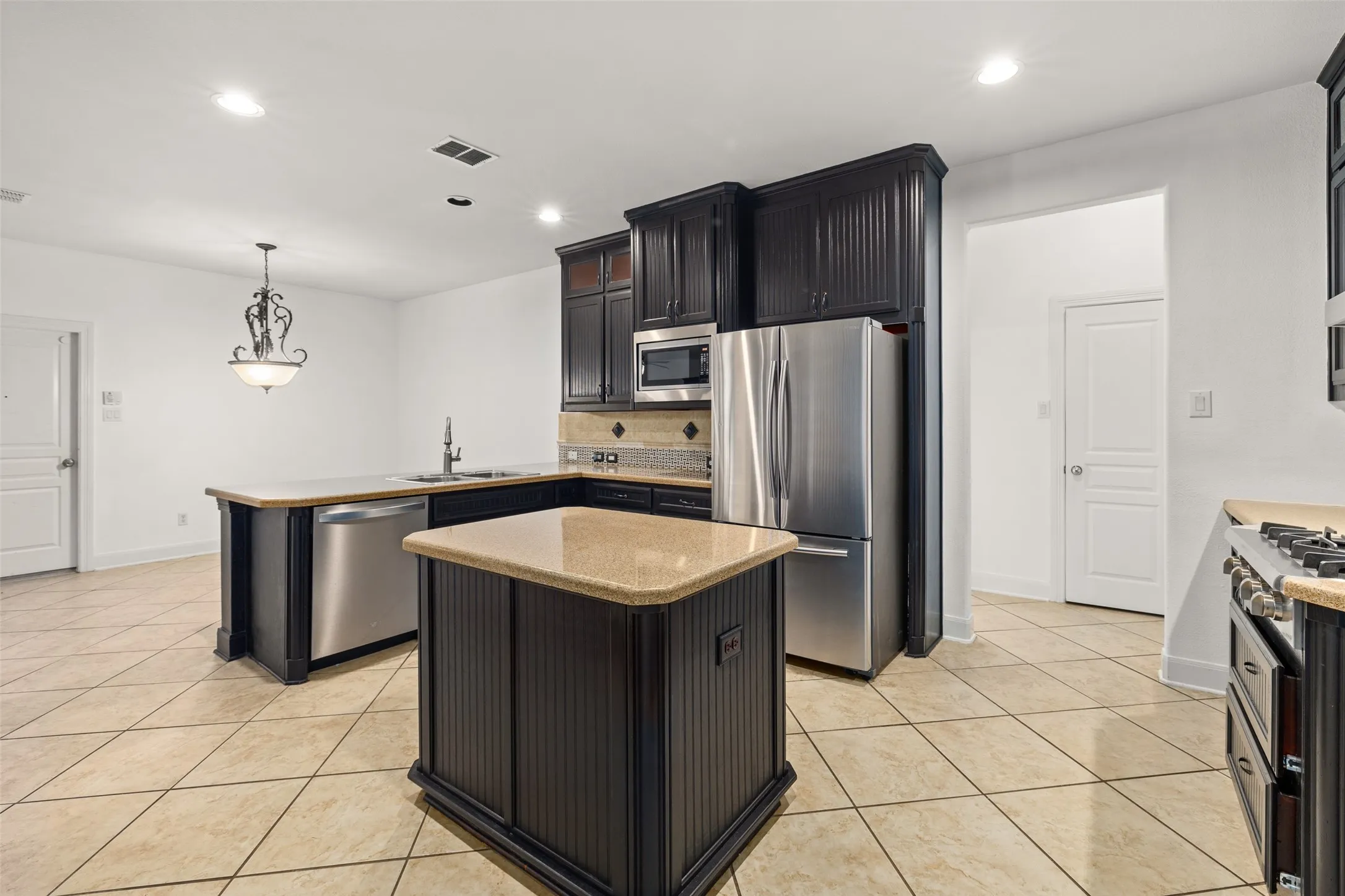 Kitchen with light tile flooring, stainless steel appliances, sink, a kitchen island, and tasteful backsplash