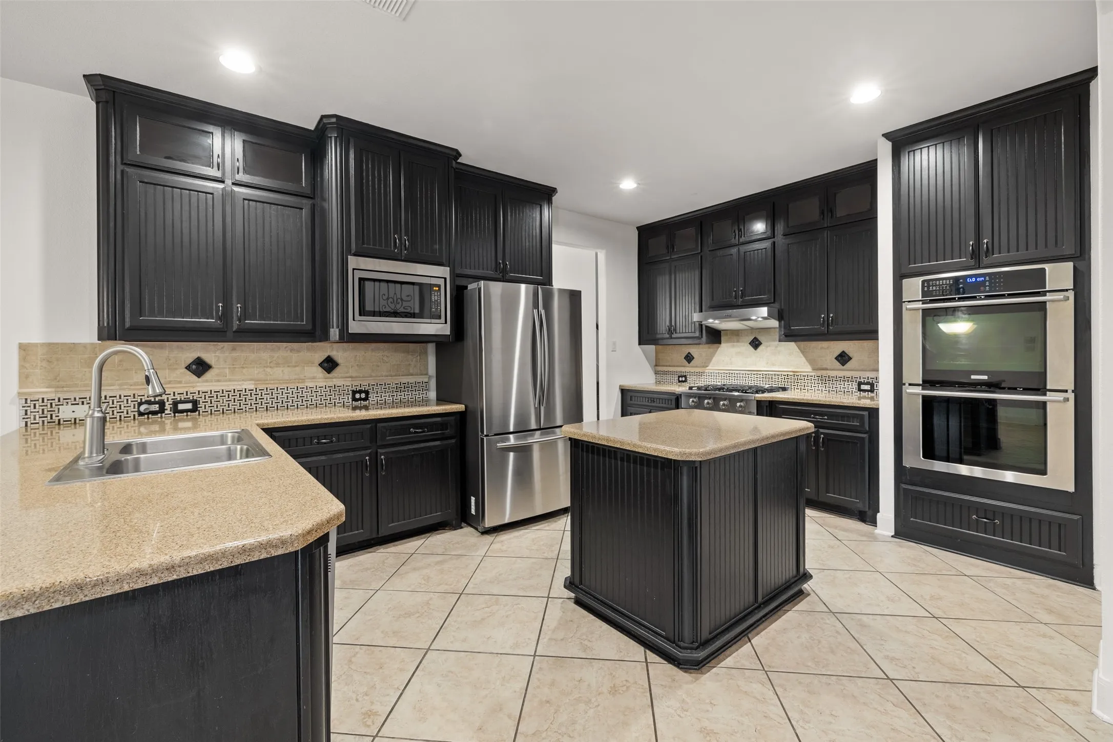 Kitchen with appliances with stainless steel finishes, light tile flooring, tasteful backsplash, sink, and a center island